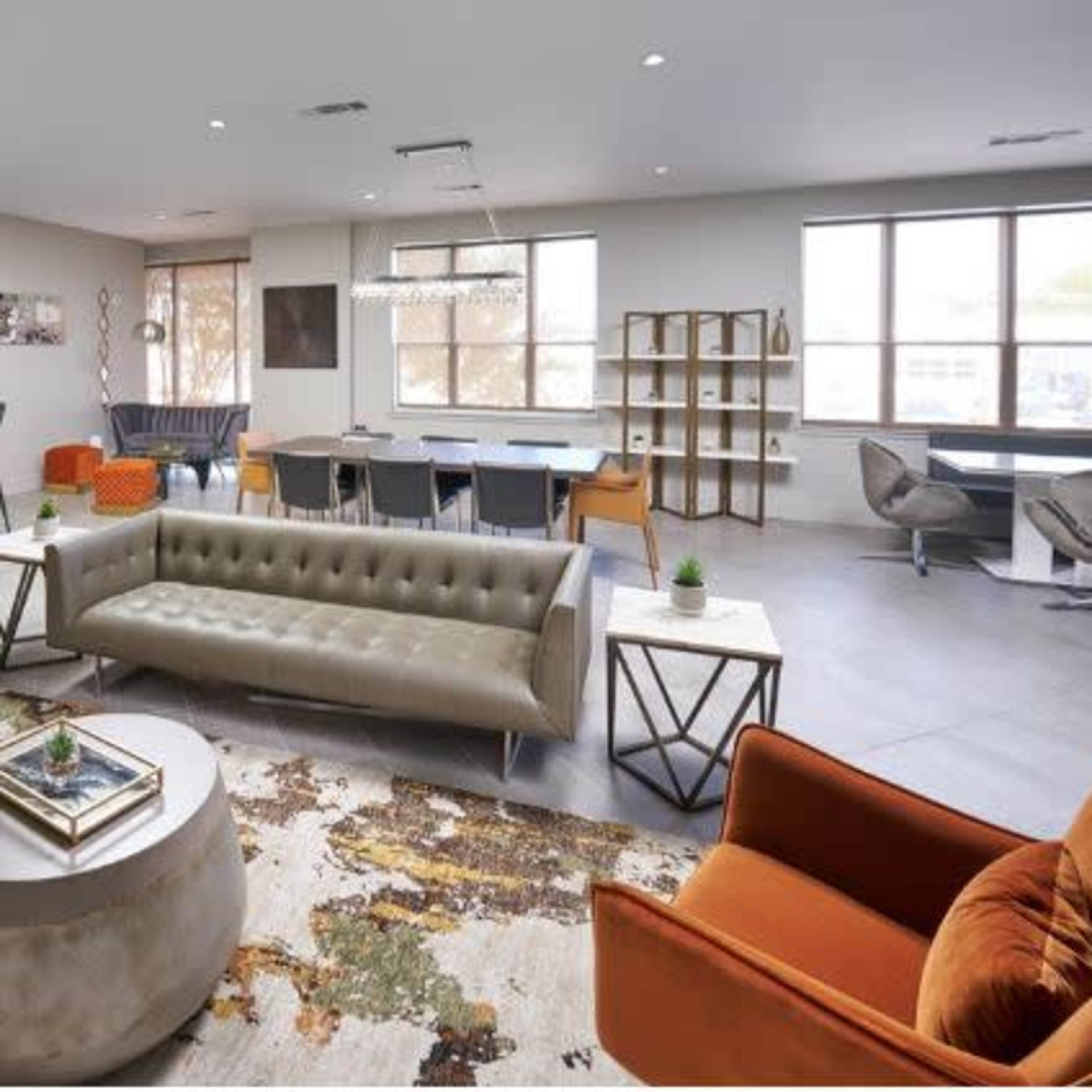 A modern living space with a gray tufted sofa, orange chairs, a round coffee table, and a dining area with a large table and various seating options.