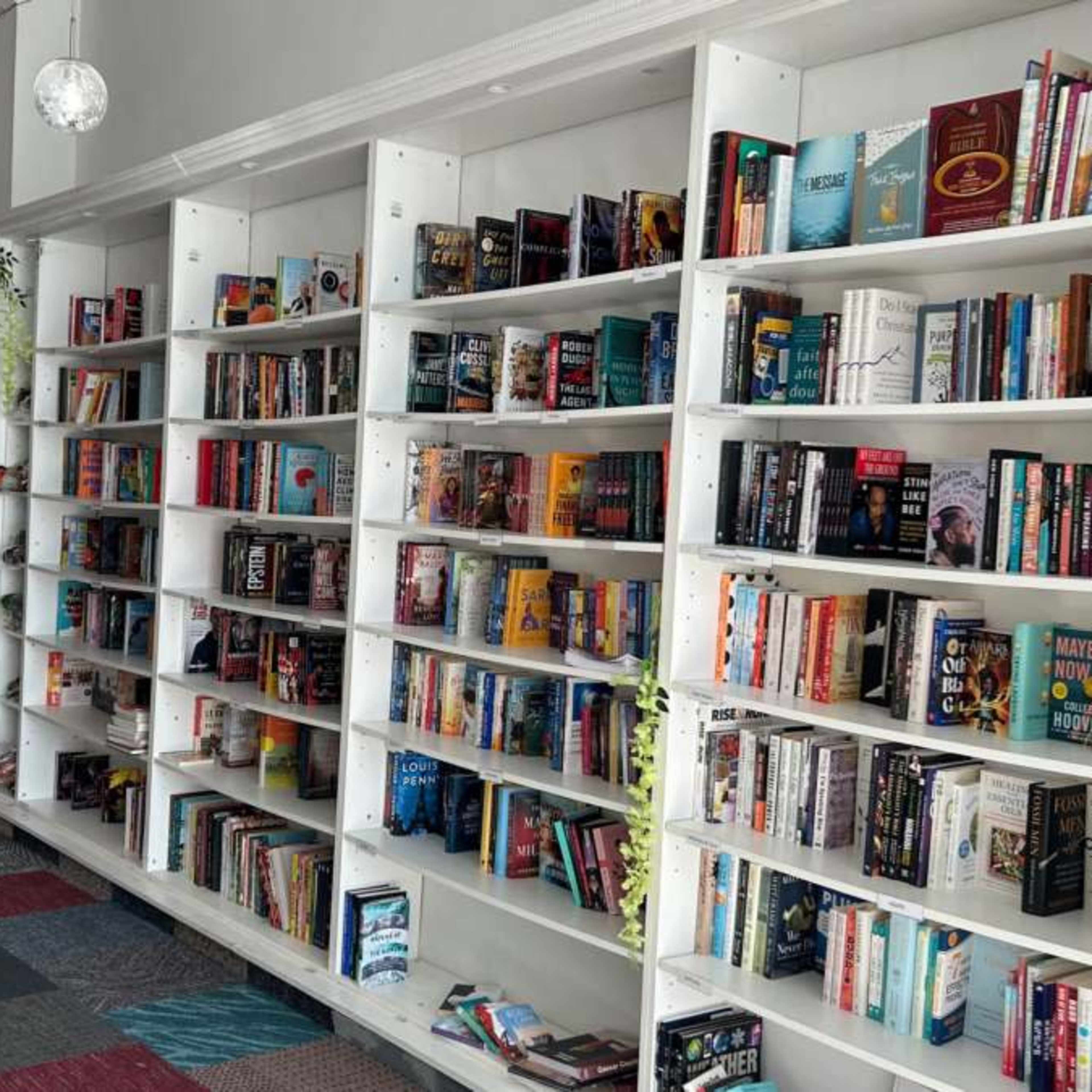 A row of white bookshelves filled with various books in a brightly lit bookstore with a tiled floor.