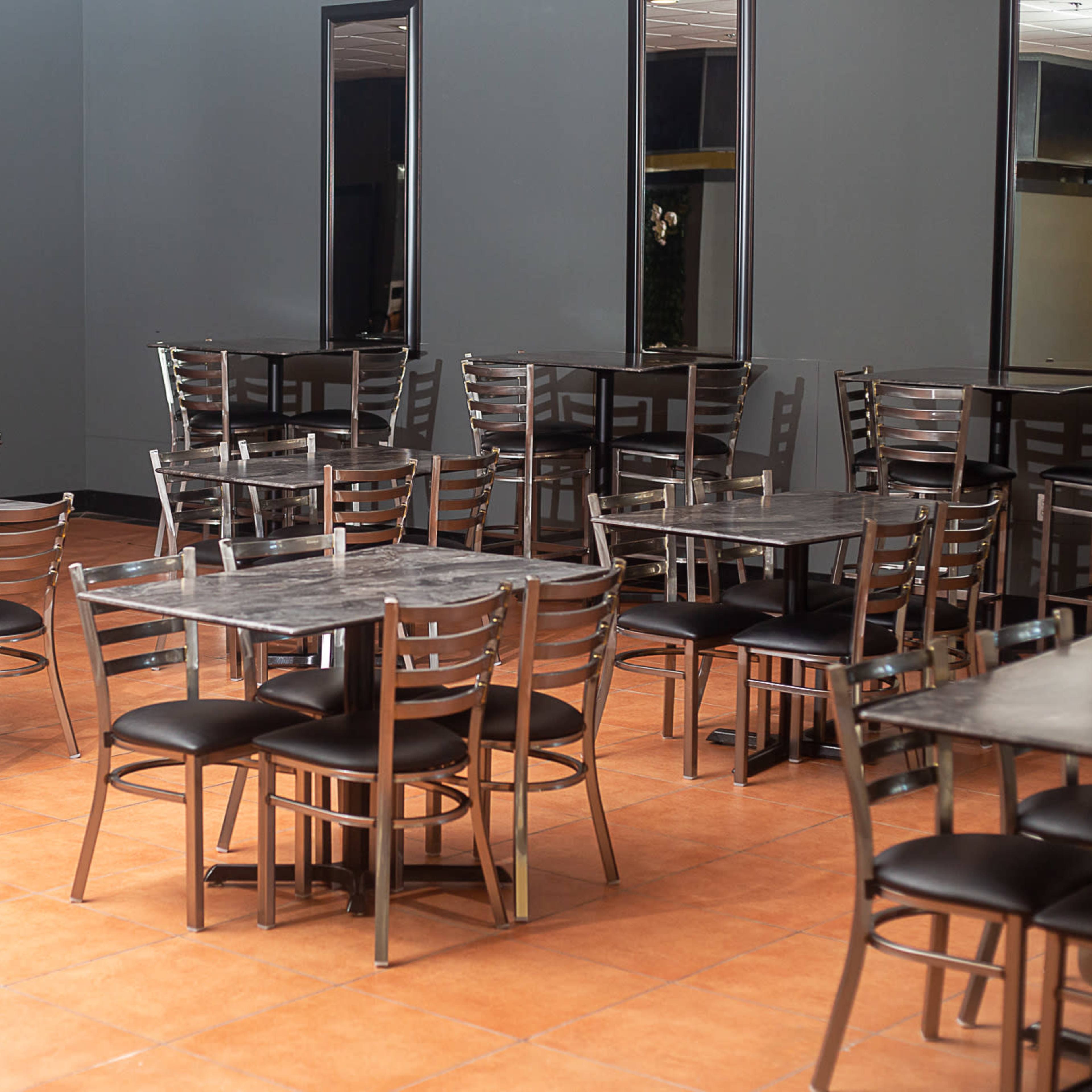 A spacious dining area with several metal-framed tables and chairs arranged on a tiled floor.