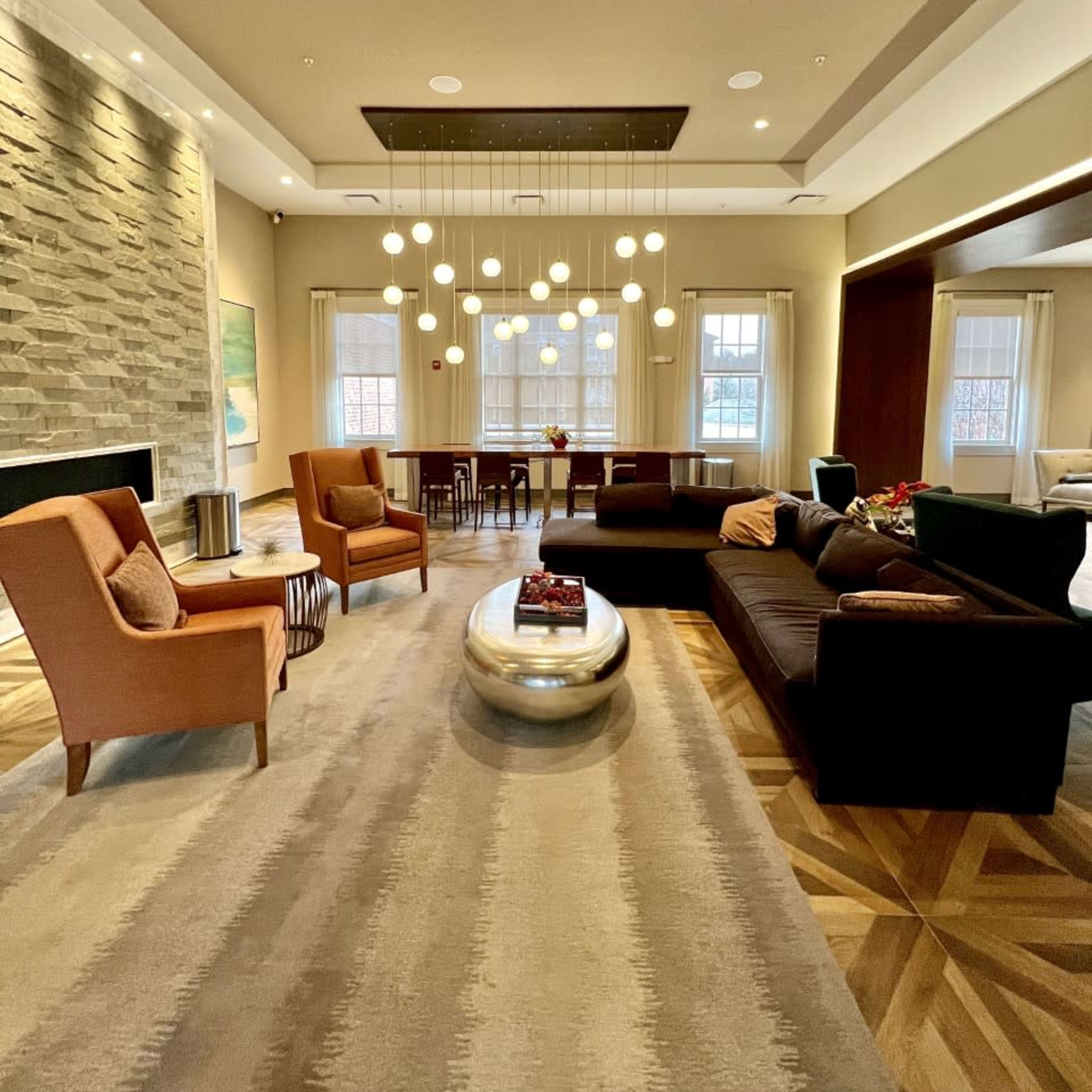 A modern living room with a stone accent wall, a central round coffee table, two armchairs, and a sectional couch, all illuminated by pendant lights above.