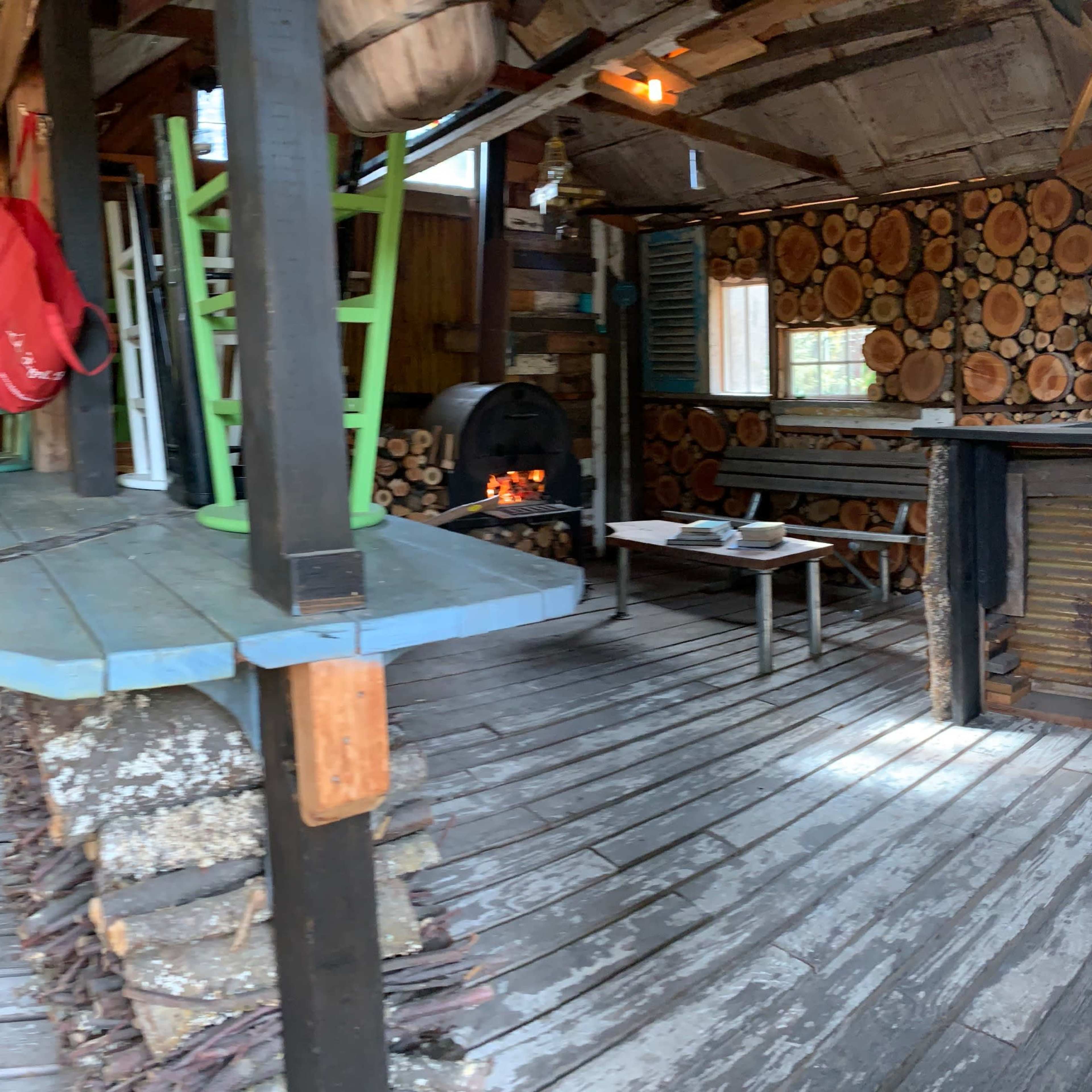 The interior of a rustic cabin features wooden walls, a stacked log accent, and various furniture pieces including a table and stove.