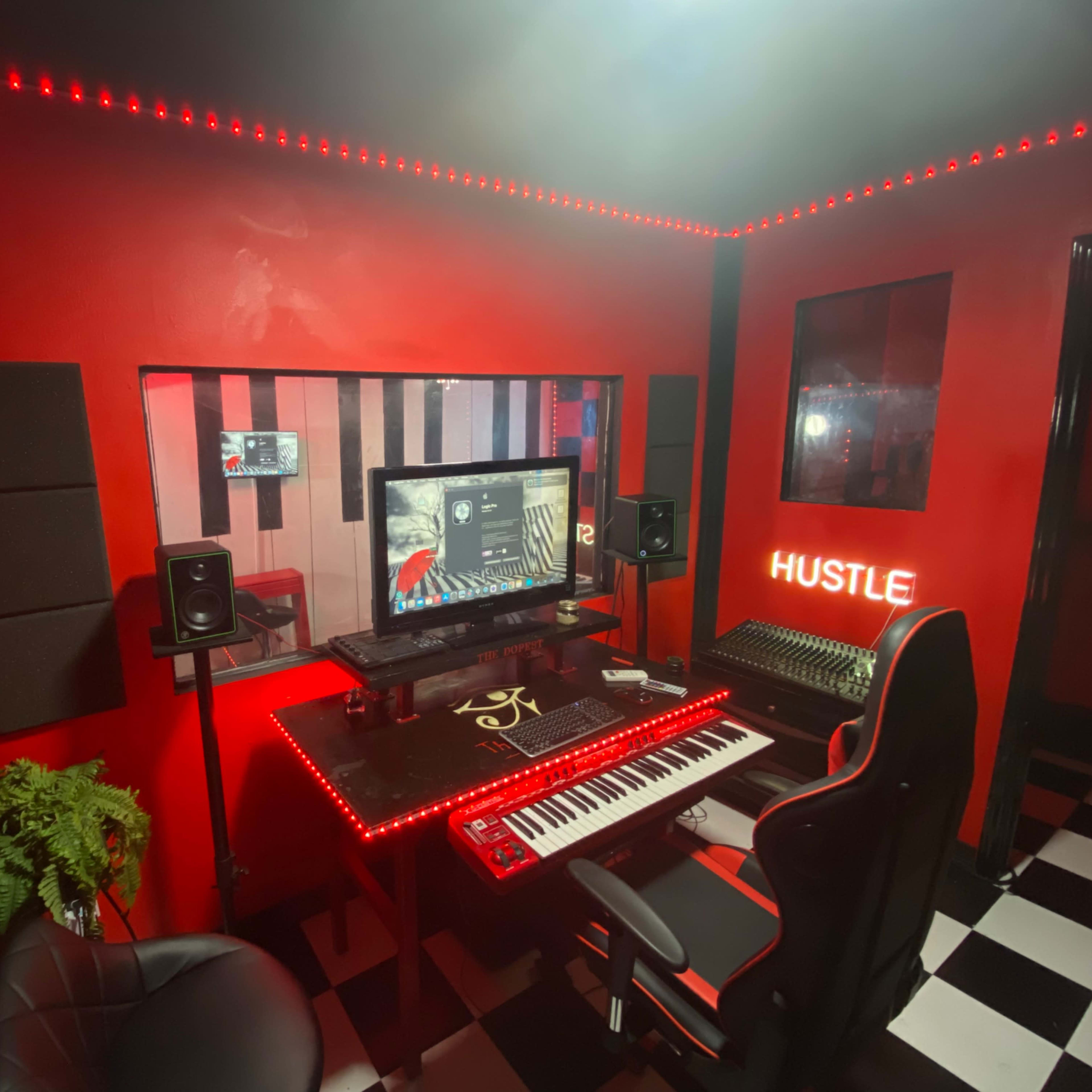 A music production studio featuring a black and red color scheme, with a computer setup, keyboard, speakers, and red LED lighting.