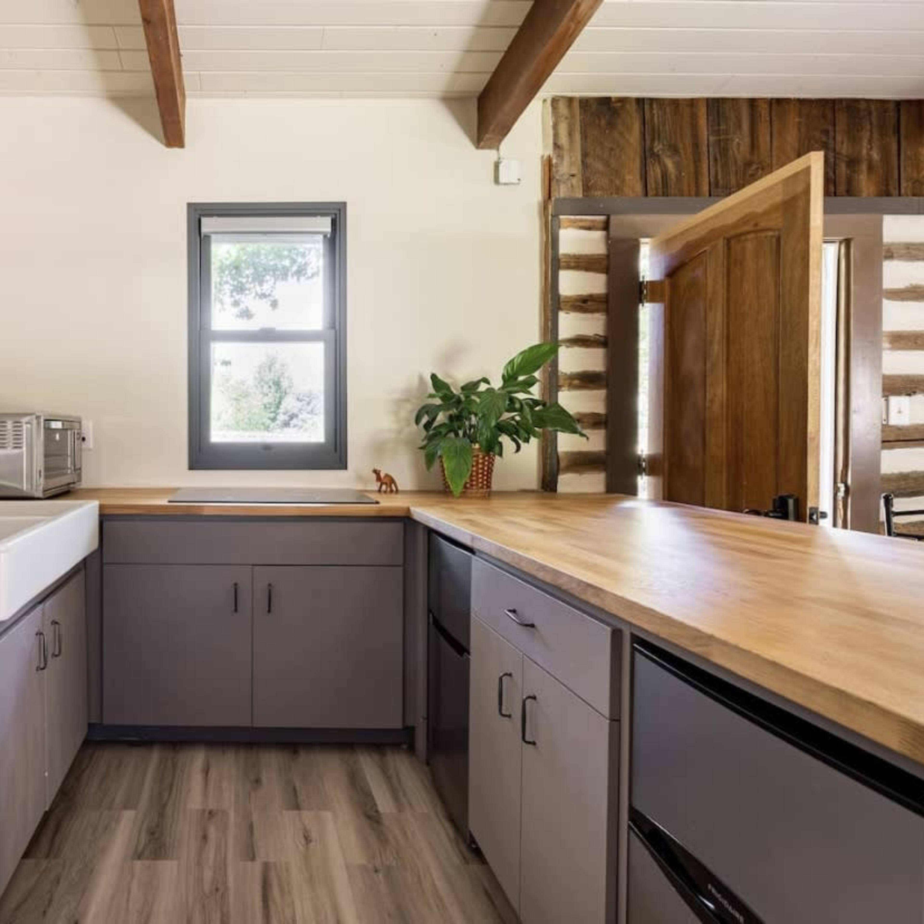 A kitchen features a washer and dryer, a large sink, wooden countertops, and a window overlooking greenery.