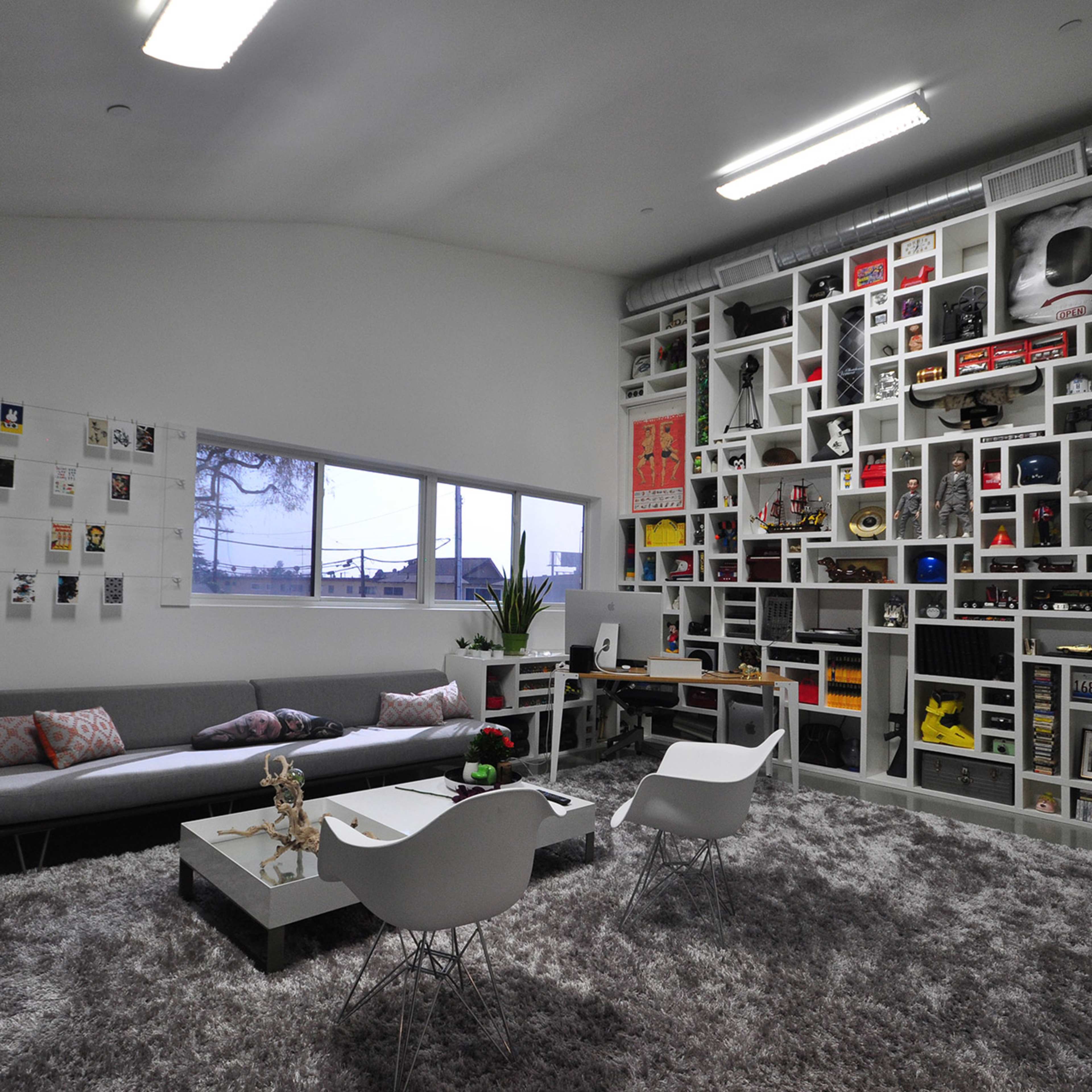 A modern living room with a gray sofa, white chairs, a coffee table, and a wall filled with various decorative items and artworks.