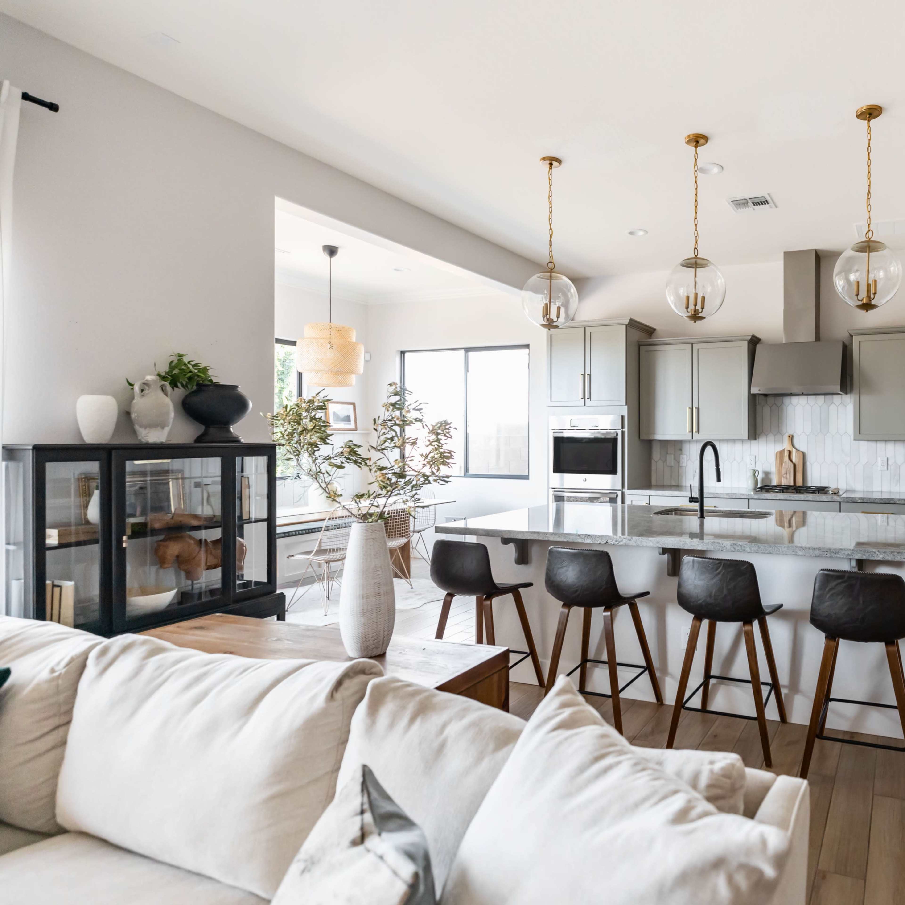 A modern kitchen features gray cabinets, a large island with bar stools, and pendant lighting above.