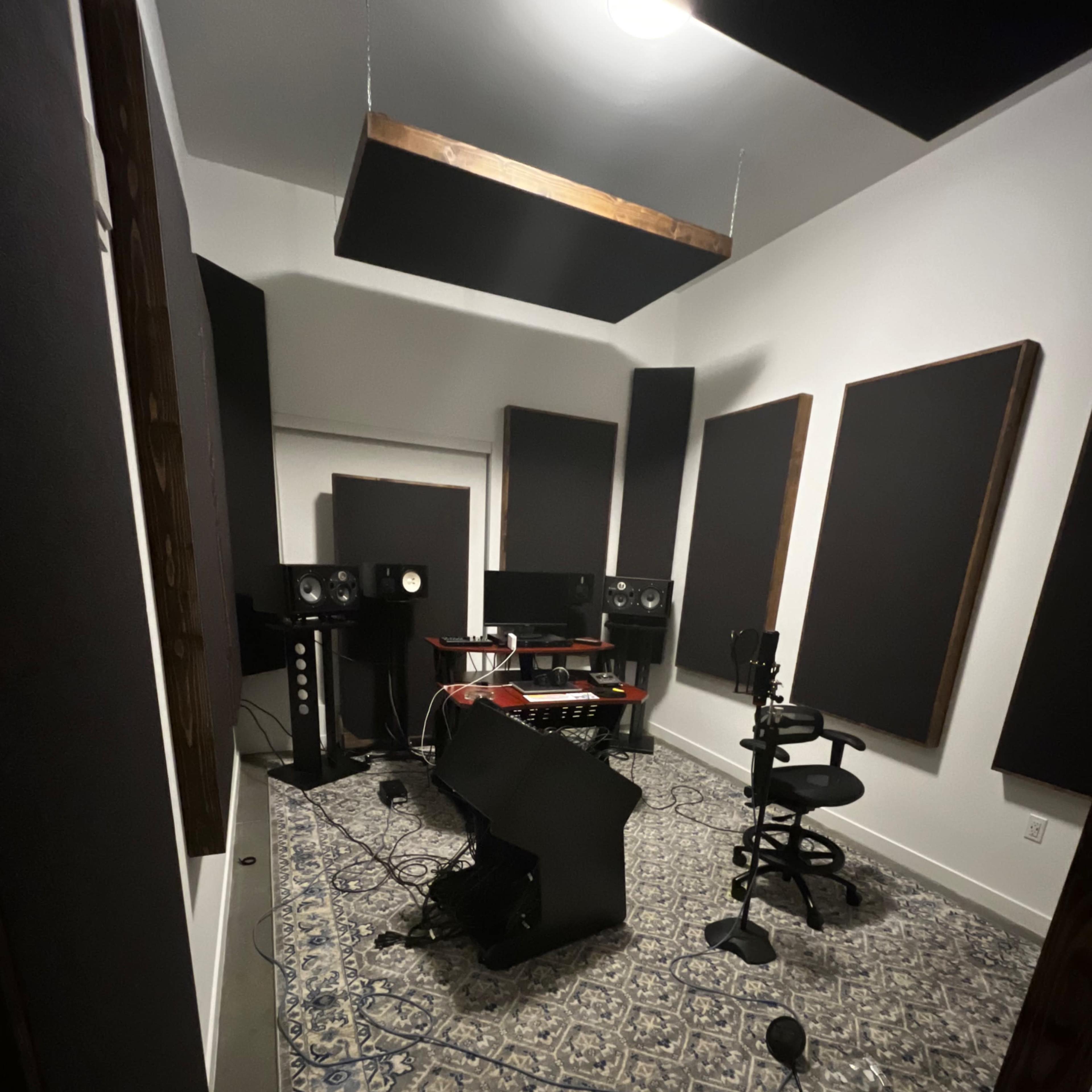 A soundproof recording studio with audio equipment, a central desk, a chair, and acoustic panels on the walls.