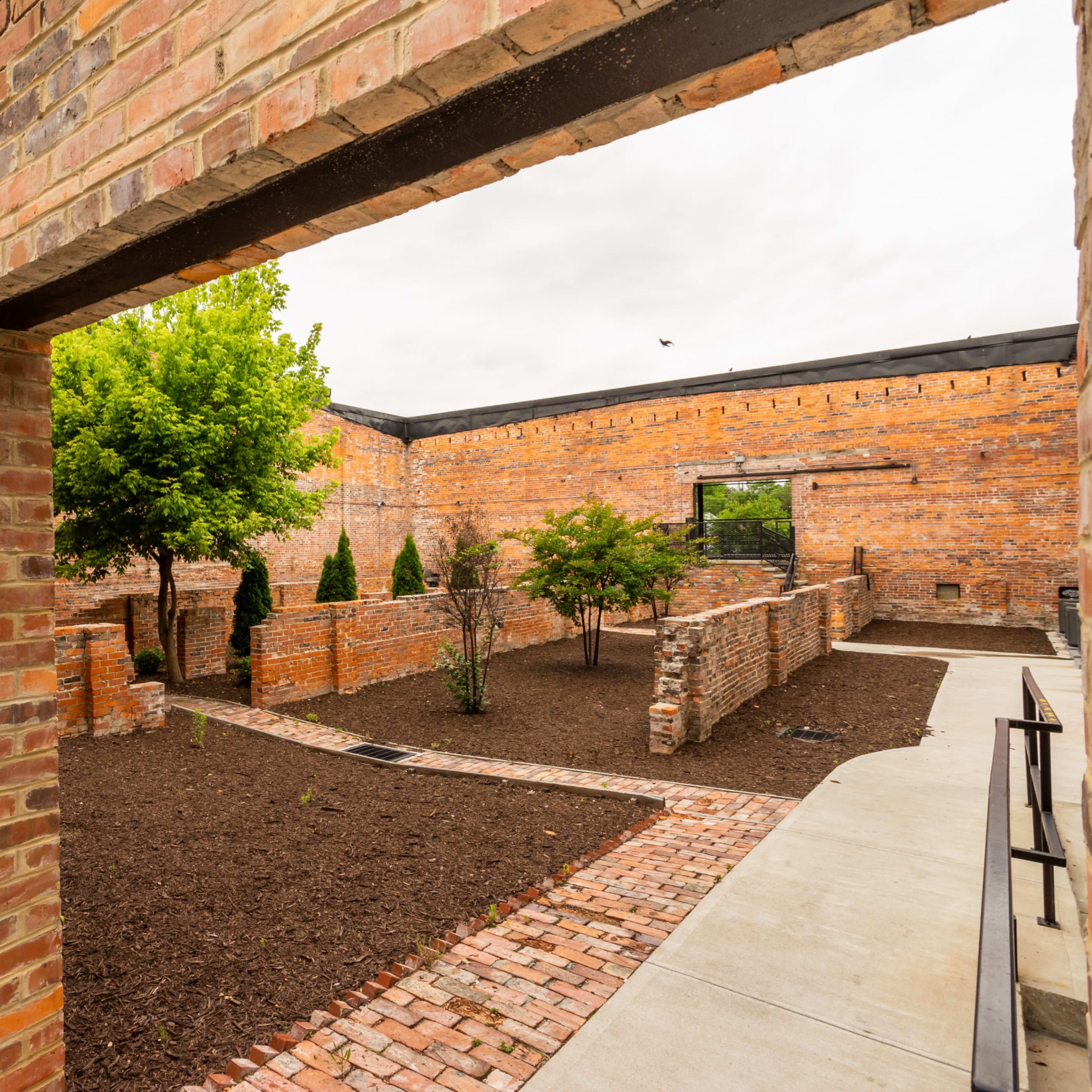 A brick building with an open archway leading to a landscaped area featuring trees and freshly laid mulch.