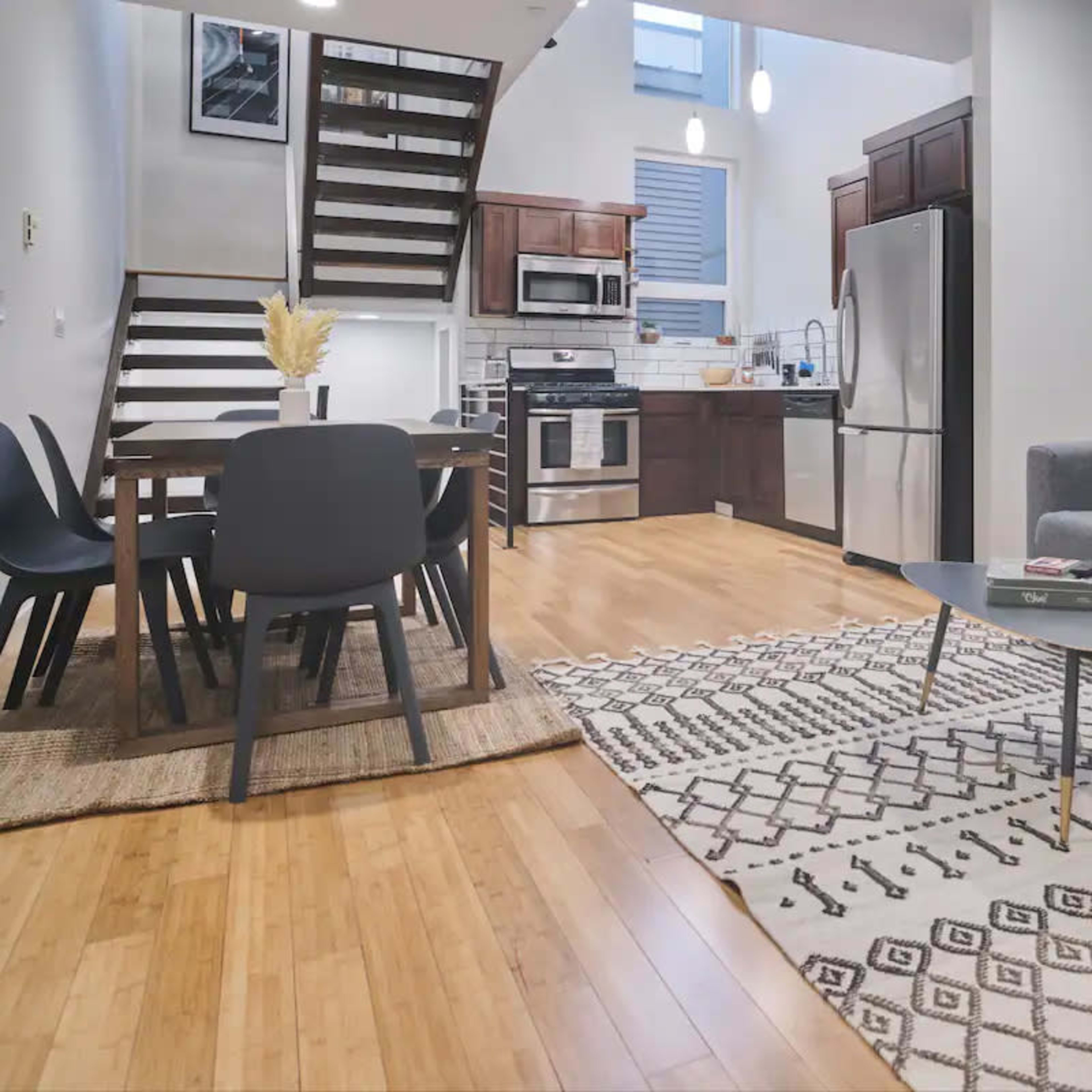 A modern open-concept kitchen and living area with a dining table, a gray sofa, and decorative wall art made of woven materials.