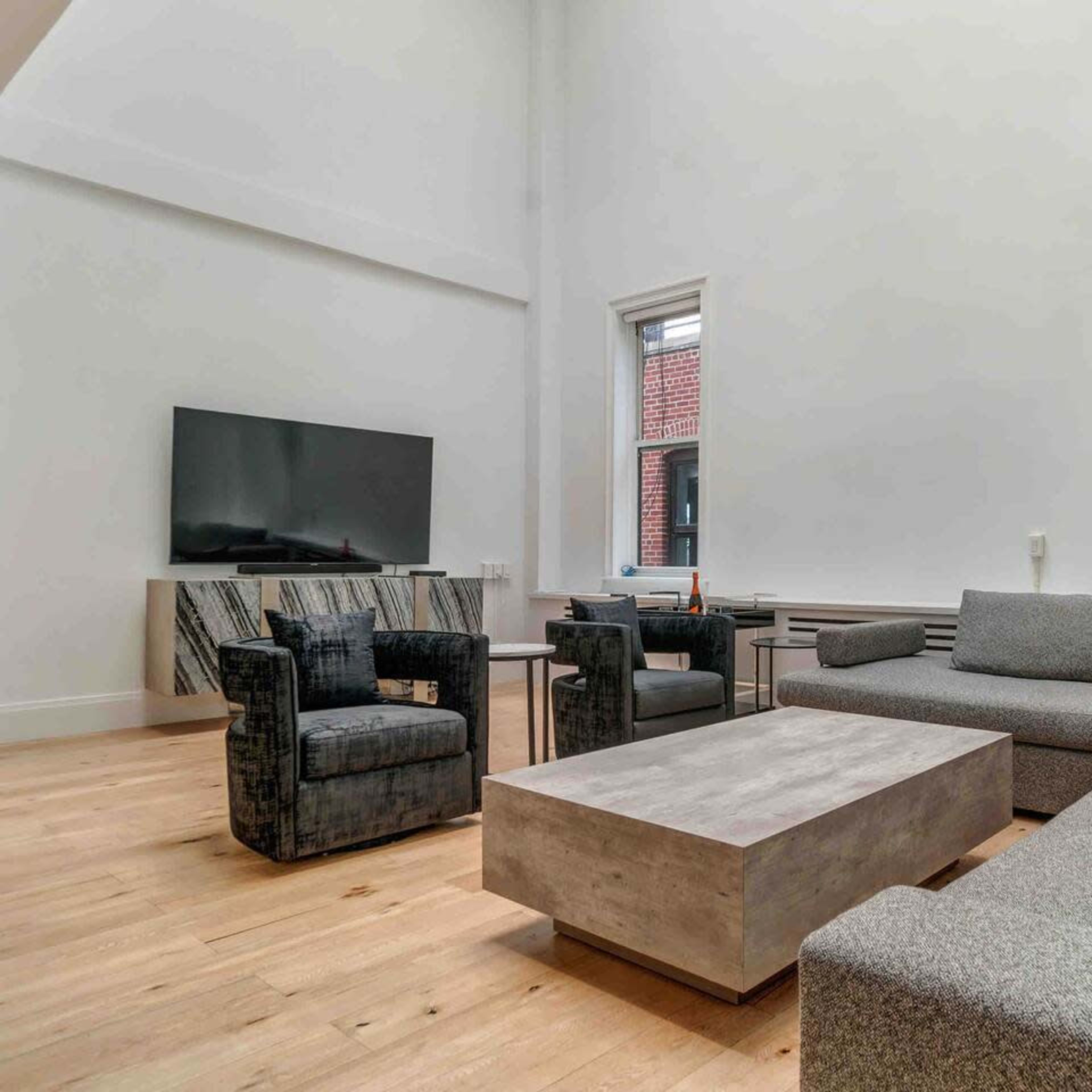 A minimalist living room featuring a large gray sectional sofa, two chairs, a coffee table, and a television mounted on the wall.