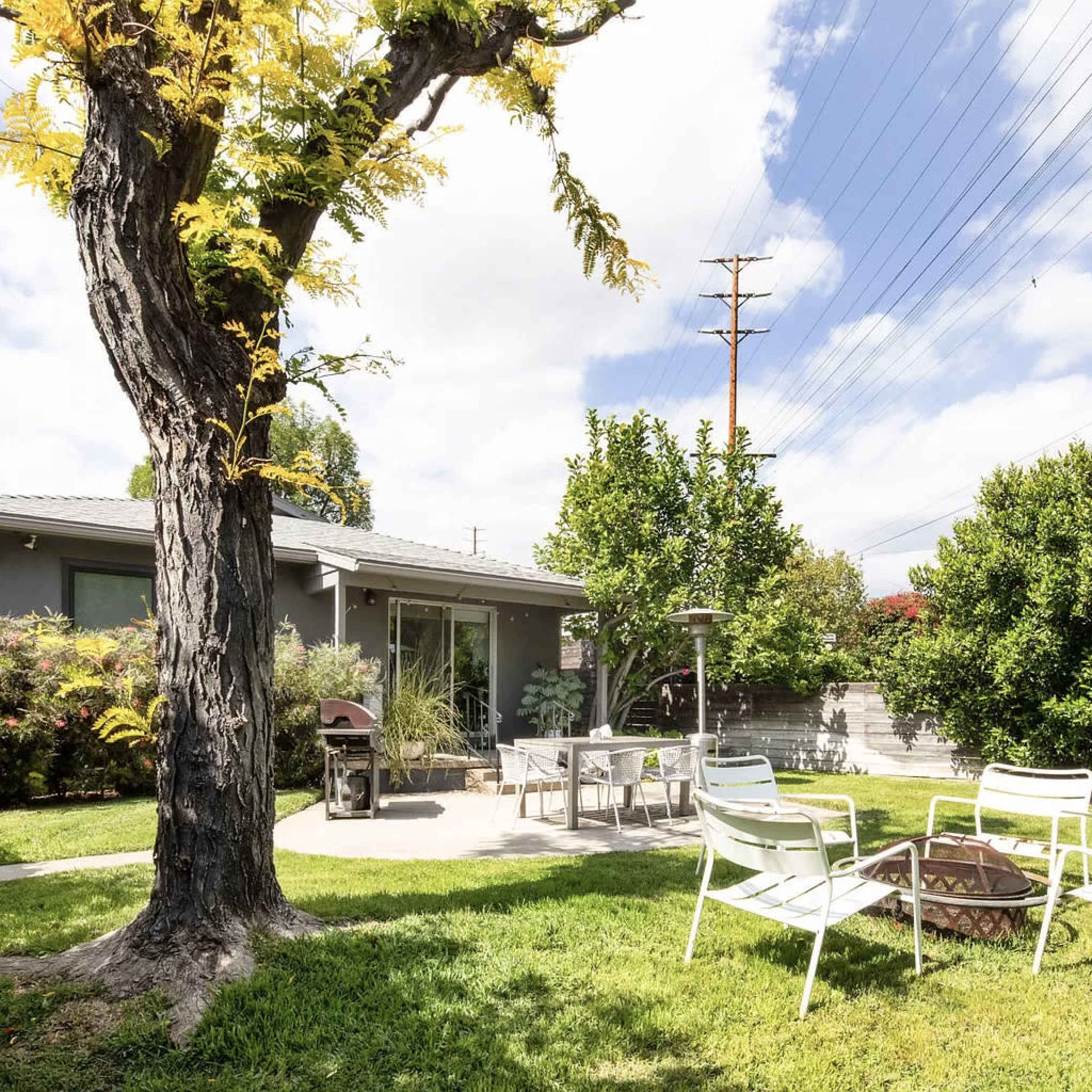 A backyard scene features a barbecue grill and seating area surrounded by greenery, with a house in the background under a partly cloudy sky.