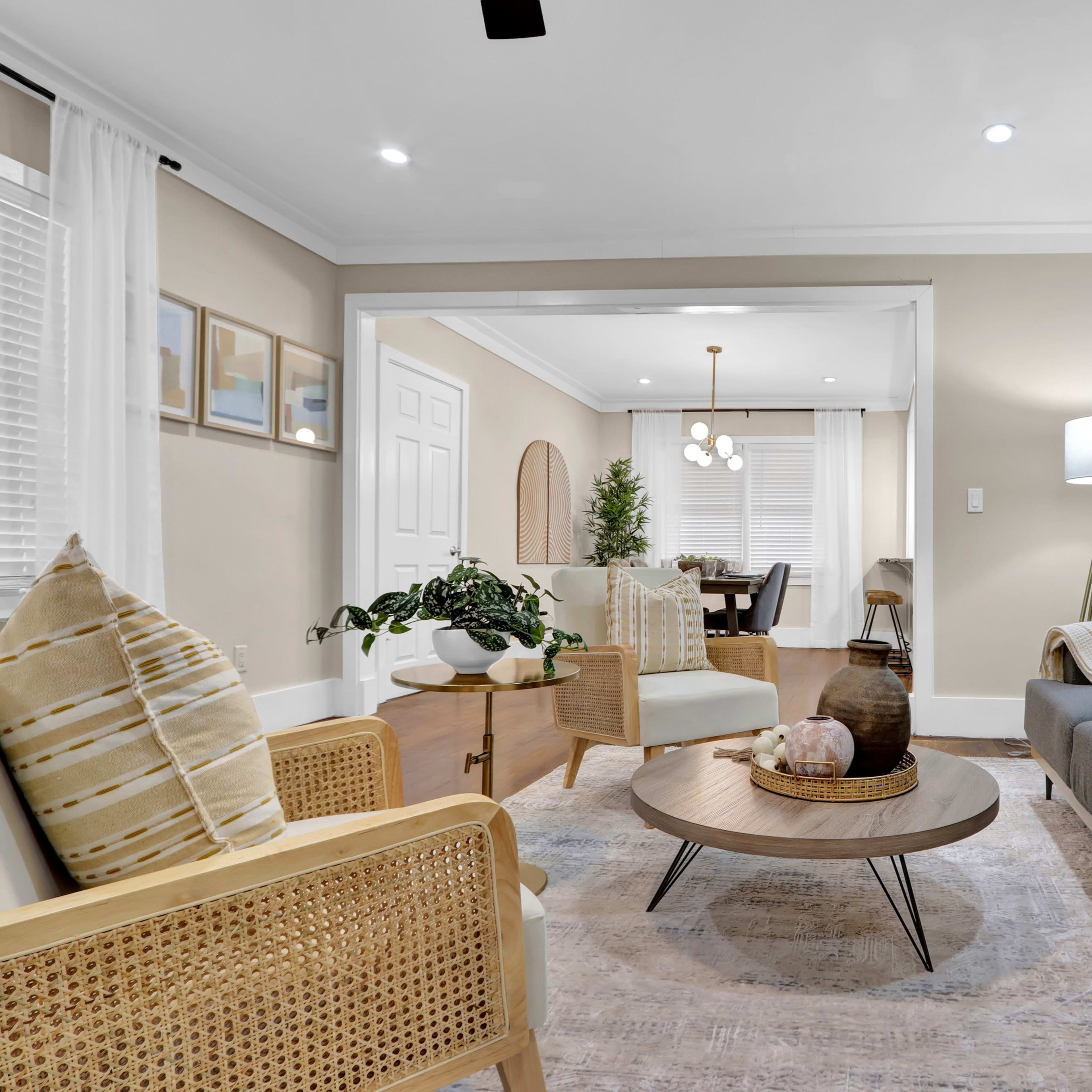A modern living room features a gray sofa, a round coffee table, and a decorative mirror on the wall, with natural light illuminating the space through large windows.