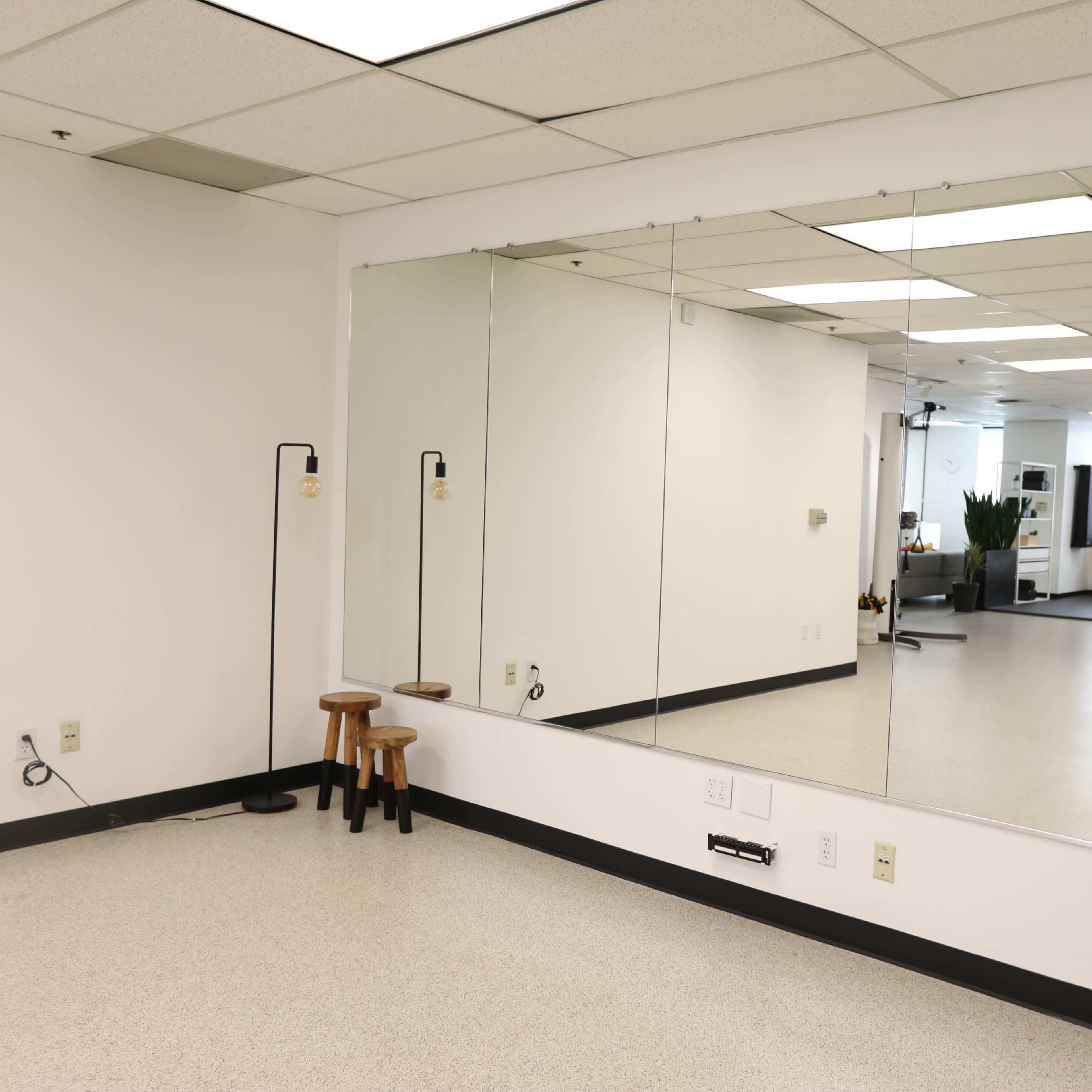 A spacious, well-lit room with mirrors on one wall, a pair of stools, and fitness equipment in the background.