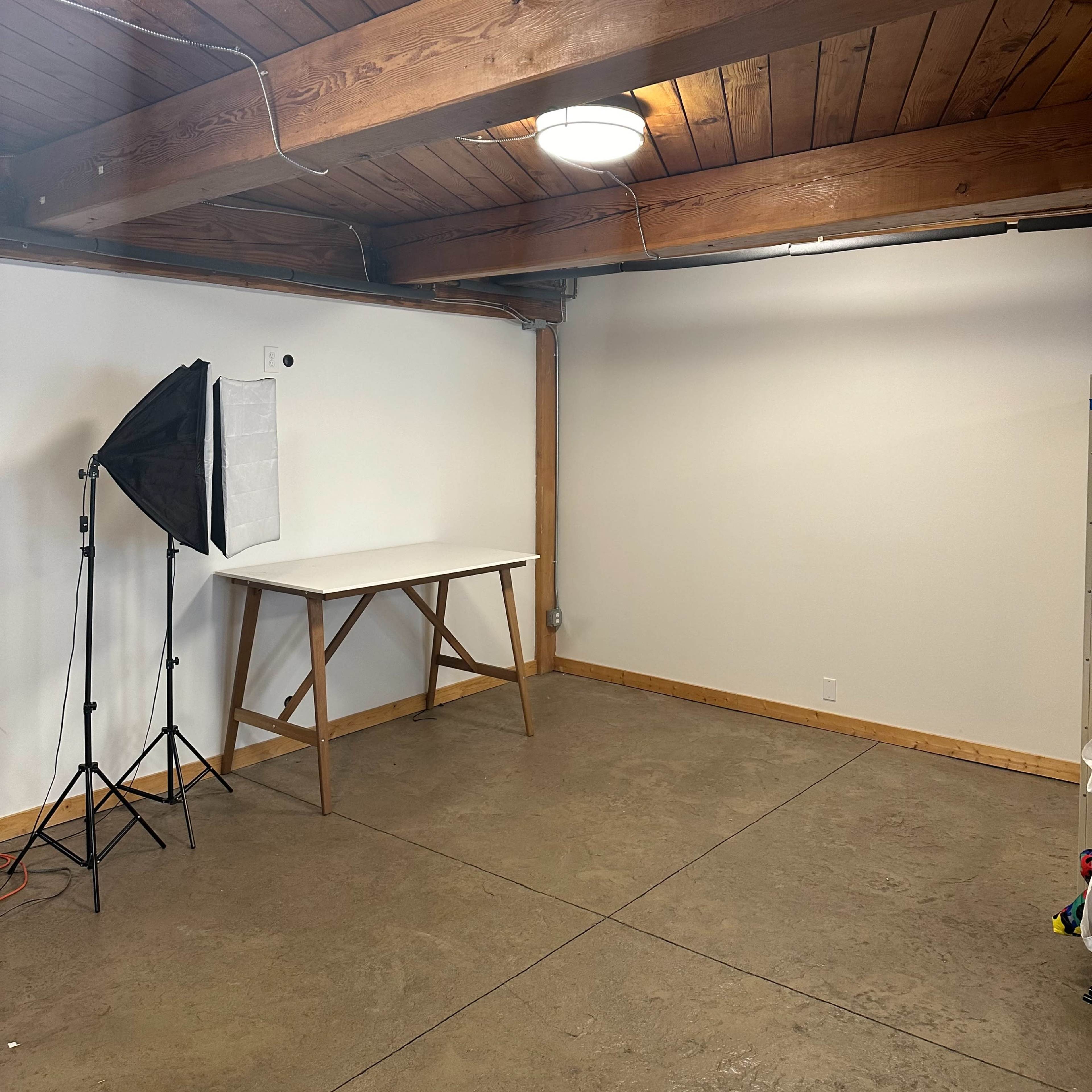 A spacious, well-lit room with a wooden ceiling, a folding table, and a light stand with a softbox.