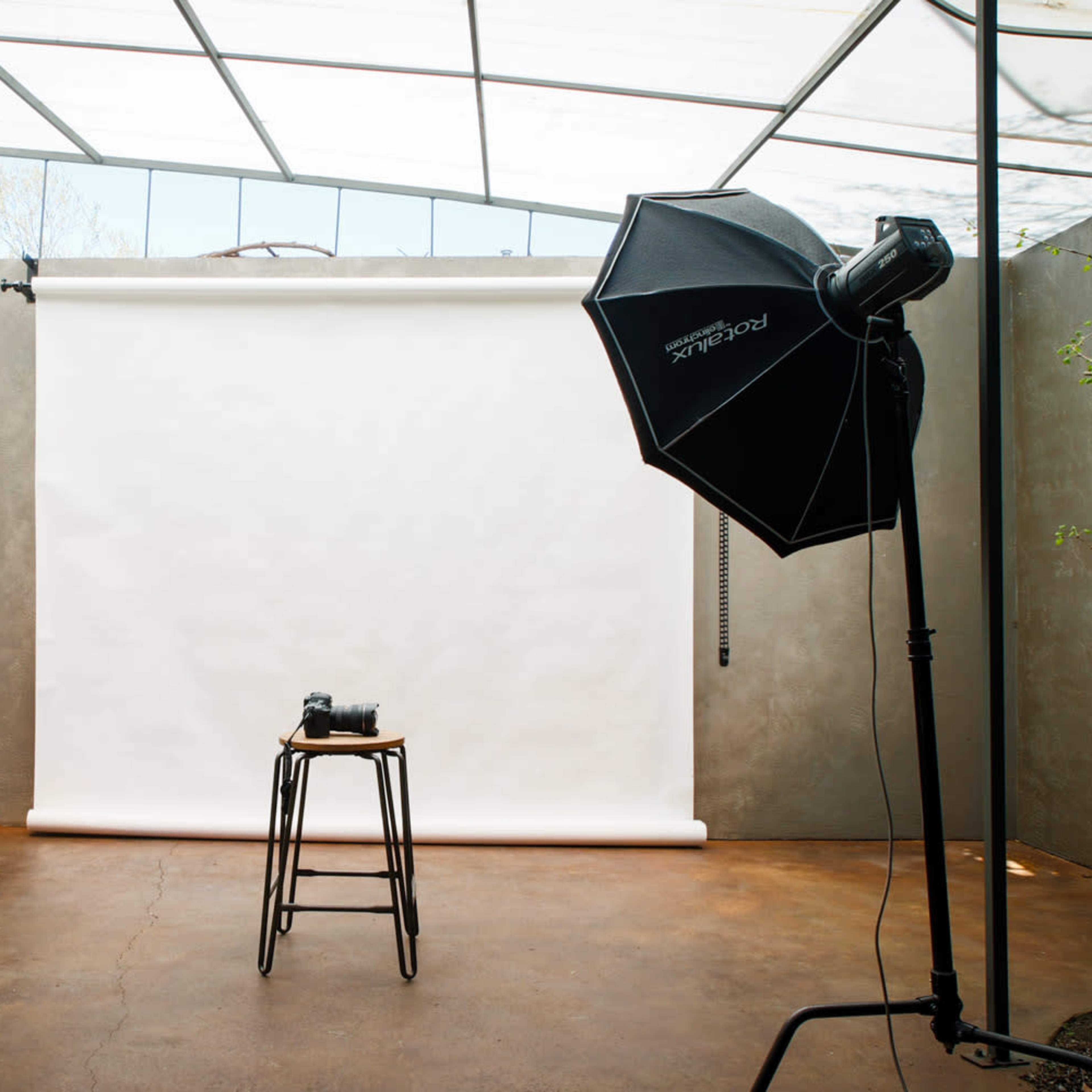 A photography studio with two lighting setups, a stool, and a blank backdrop.