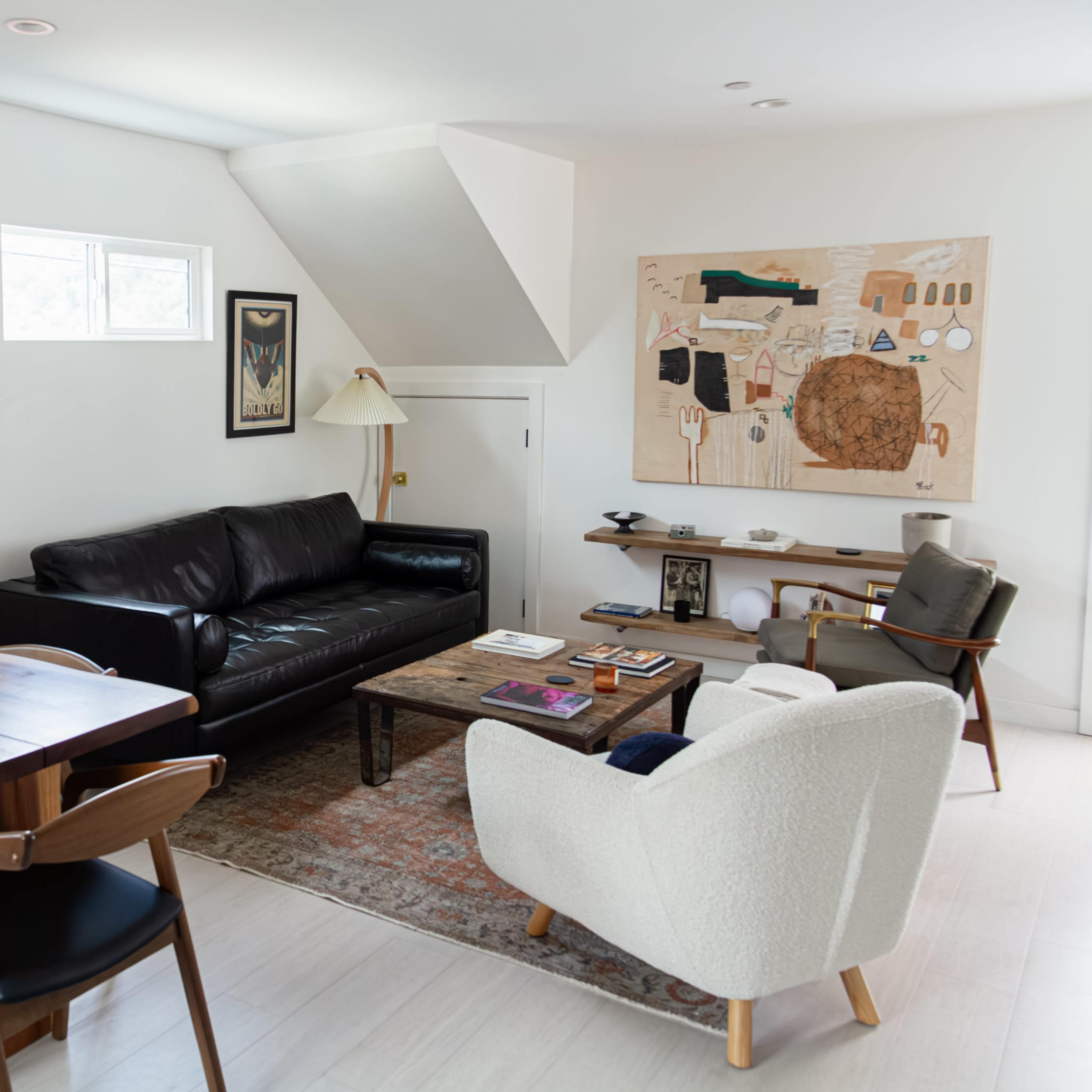 A modern living room featuring a black leather sofa, a wooden dining table with chairs, and decorative art on the white walls.