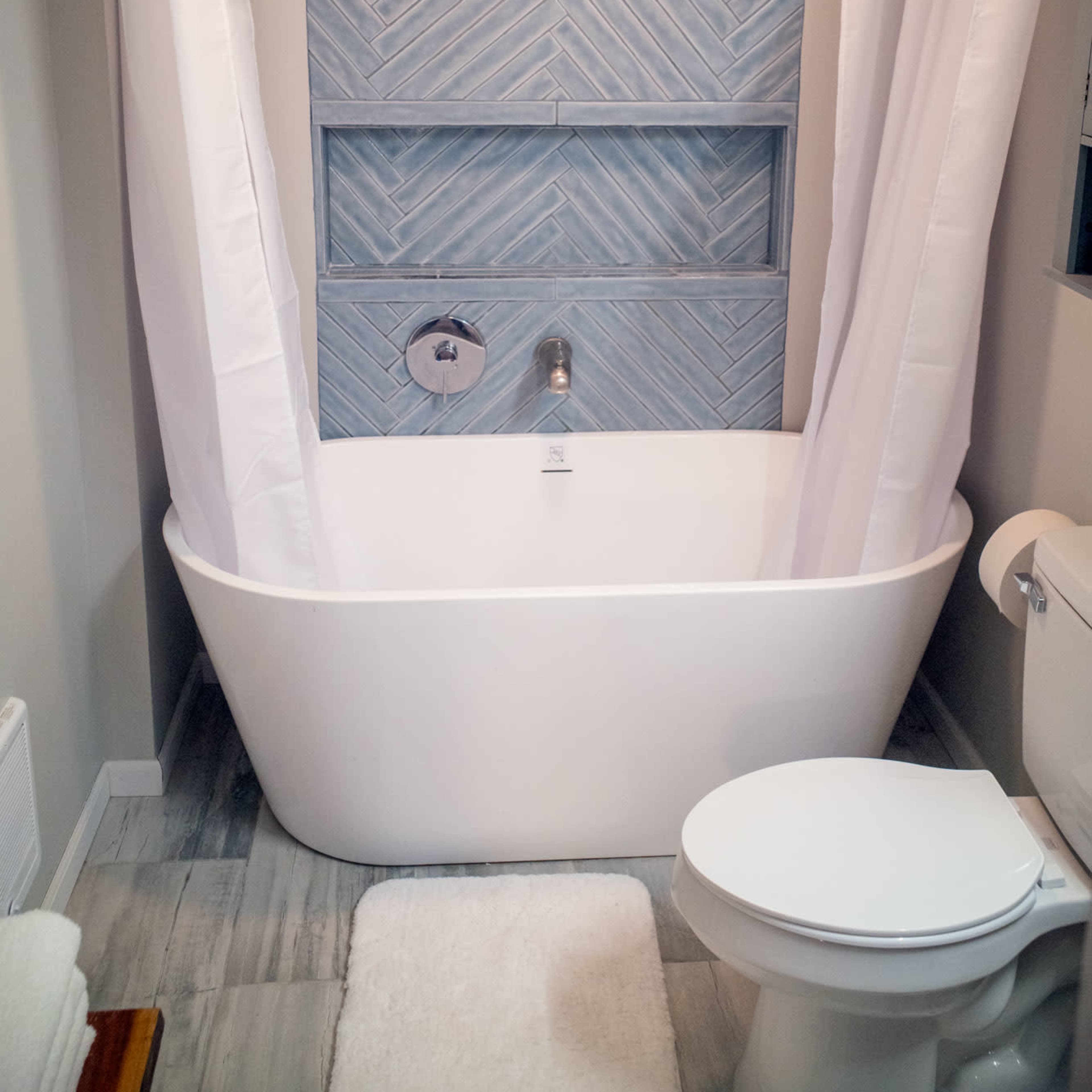 A bathroom featuring a freestanding white bathtub, a blue chevron-patterned accent wall, and a toilet beside it.