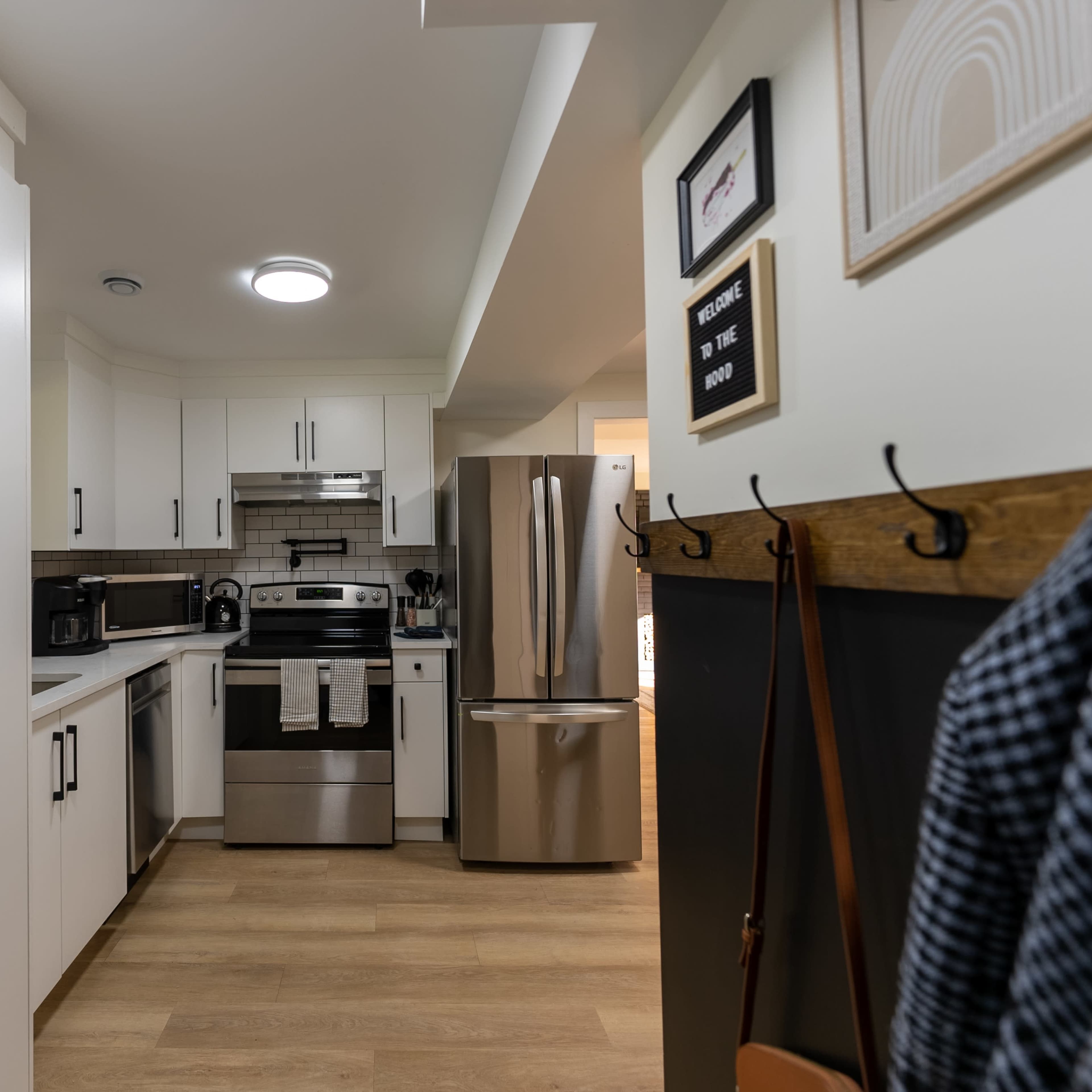 A modern kitchen with white cabinets, stainless steel appliances, and light wood flooring.