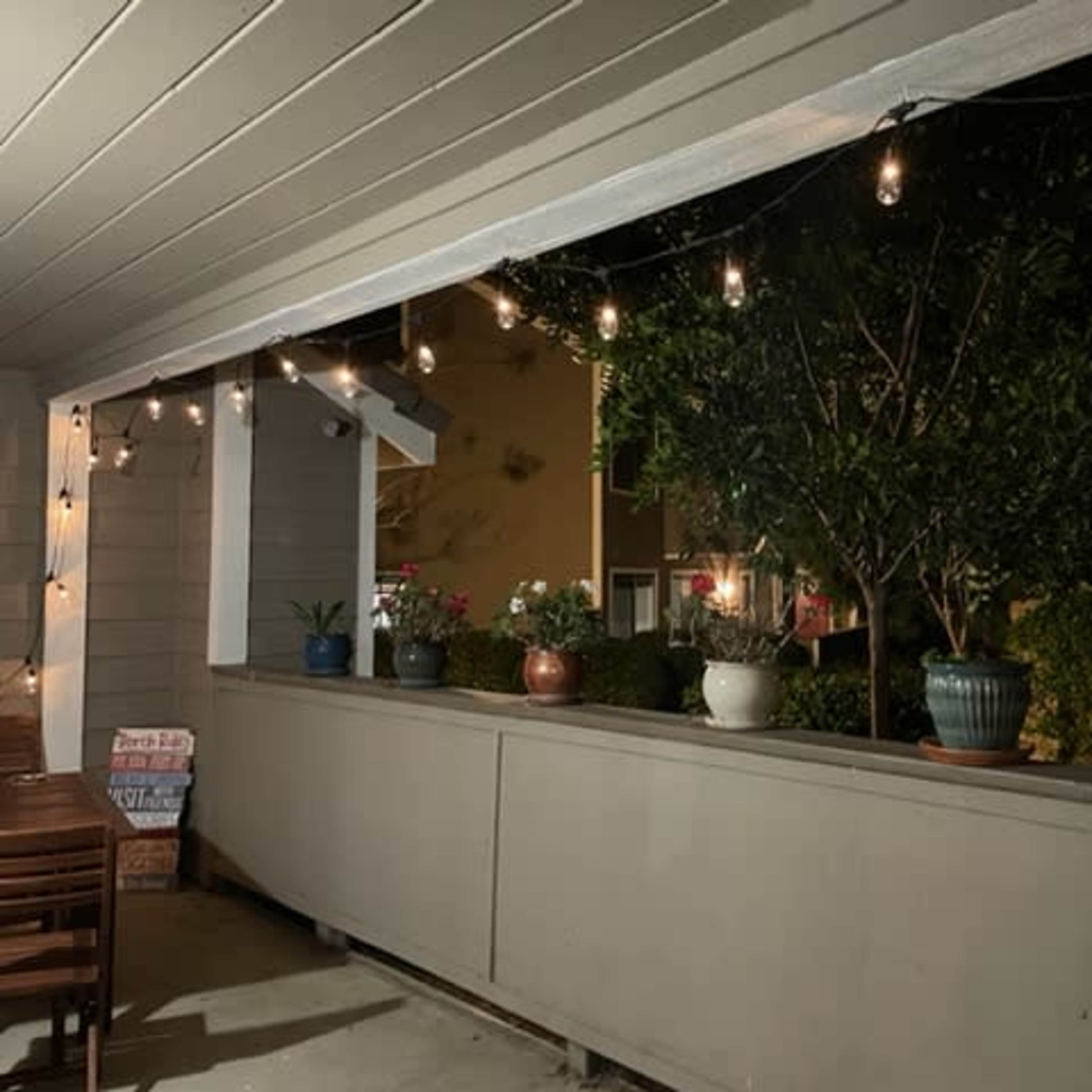A porch area is illuminated by string lights, featuring potted plants along a railing.