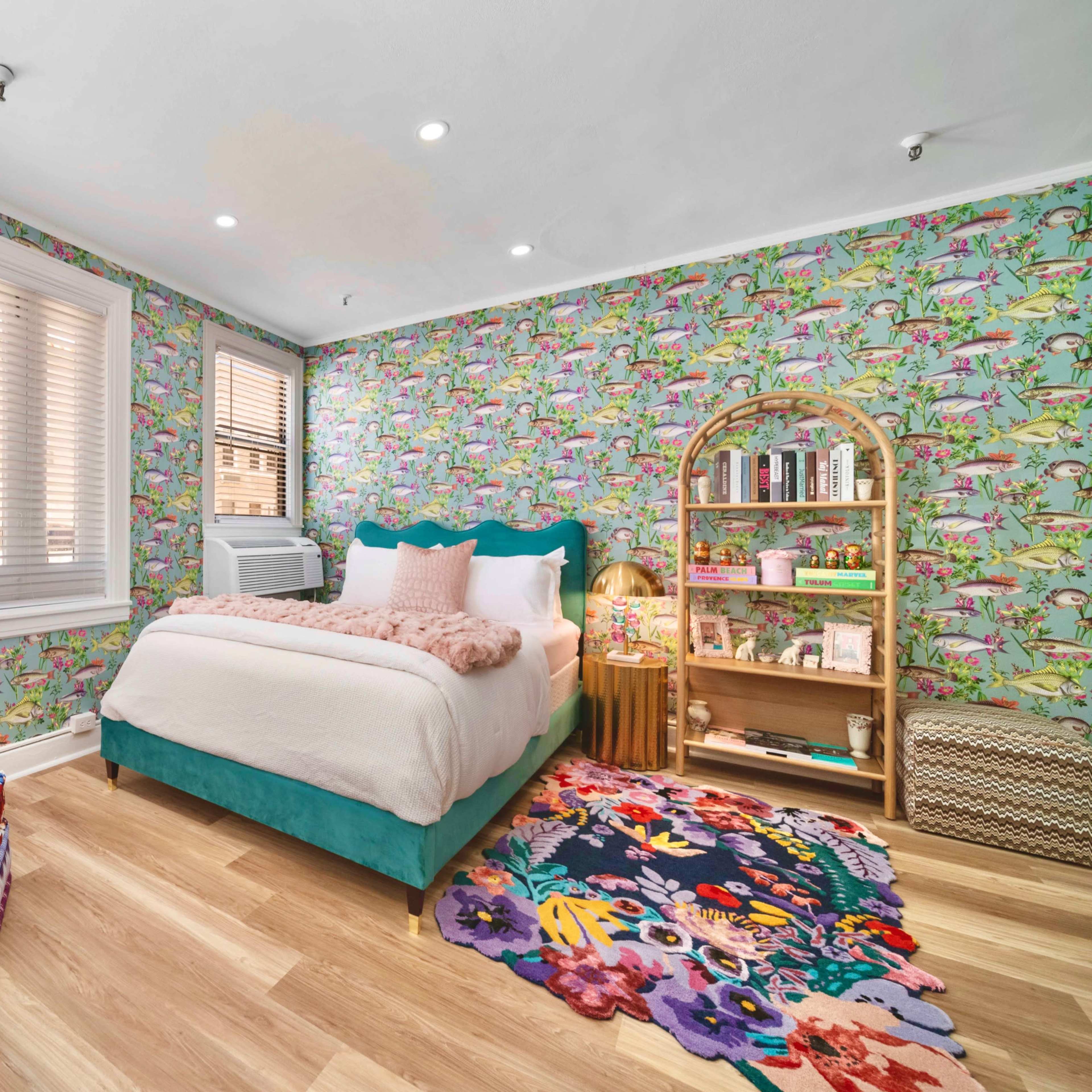 A brightly decorated bedroom with floral wallpaper, a turquoise bed, and a shelf filled with books and decorative items.