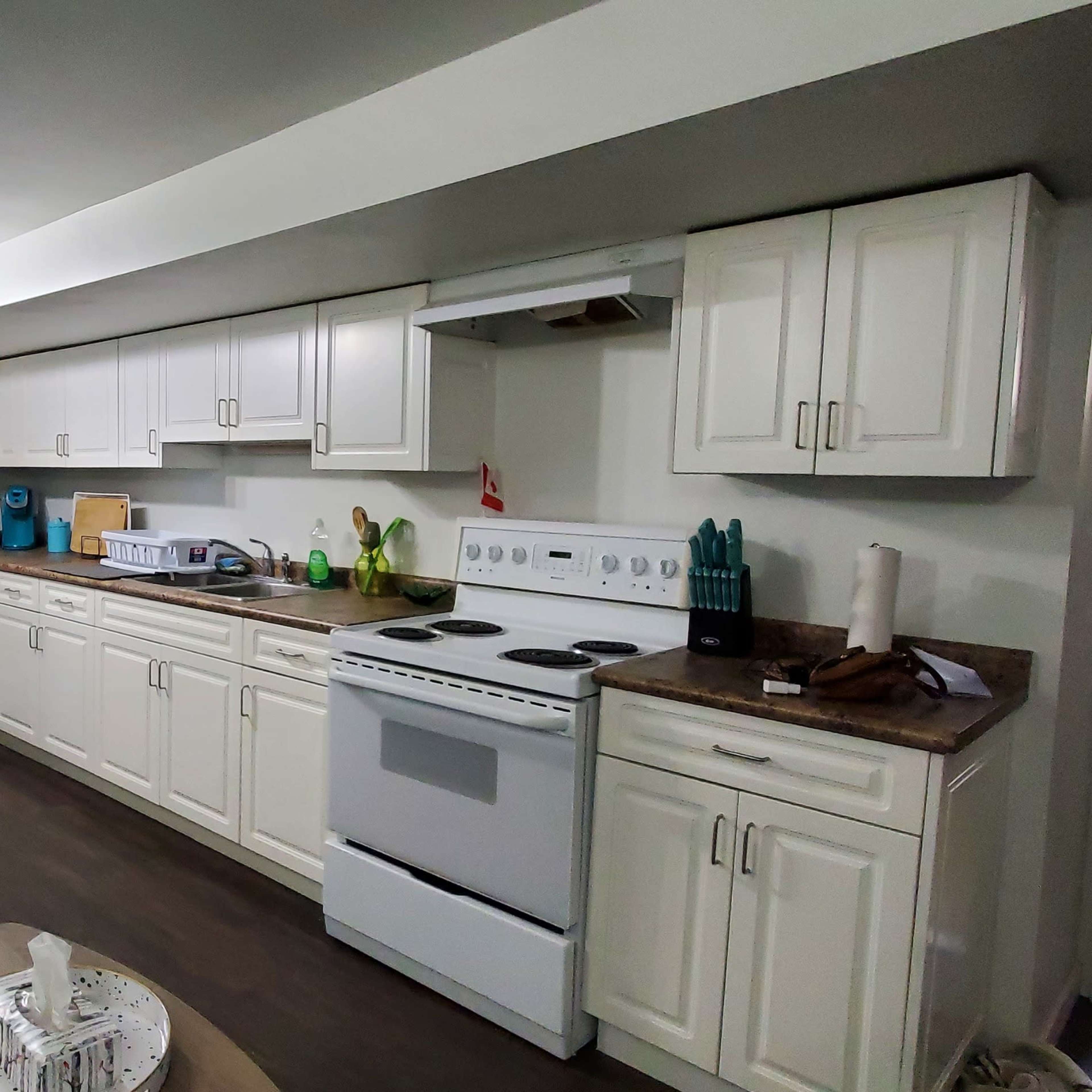 A modern kitchen with white cabinetry, a stove, a fridge, and a small seating area with a blue couch.