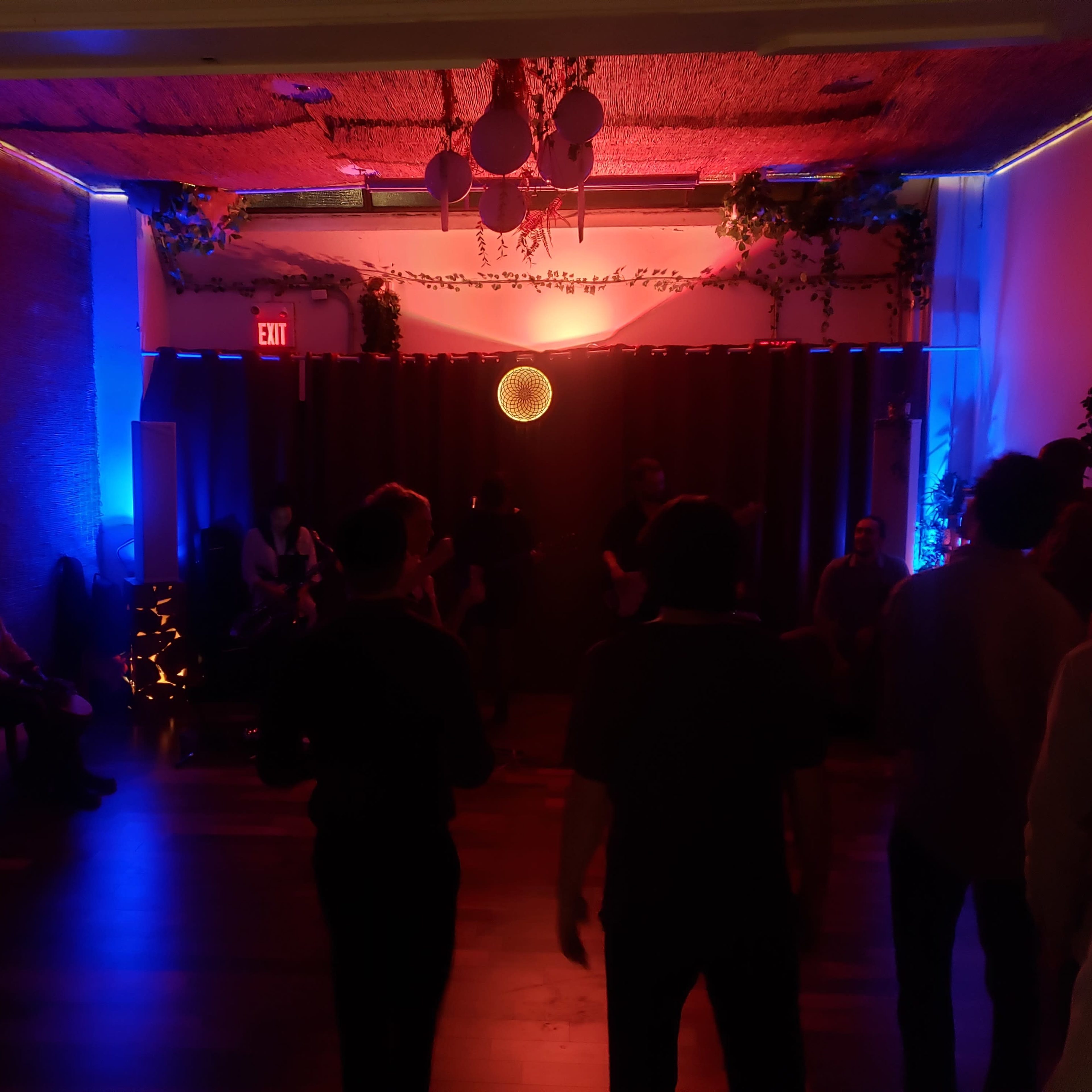 A crowd gathers in a dimly lit room adorned with colorful lights and decorations for an event.