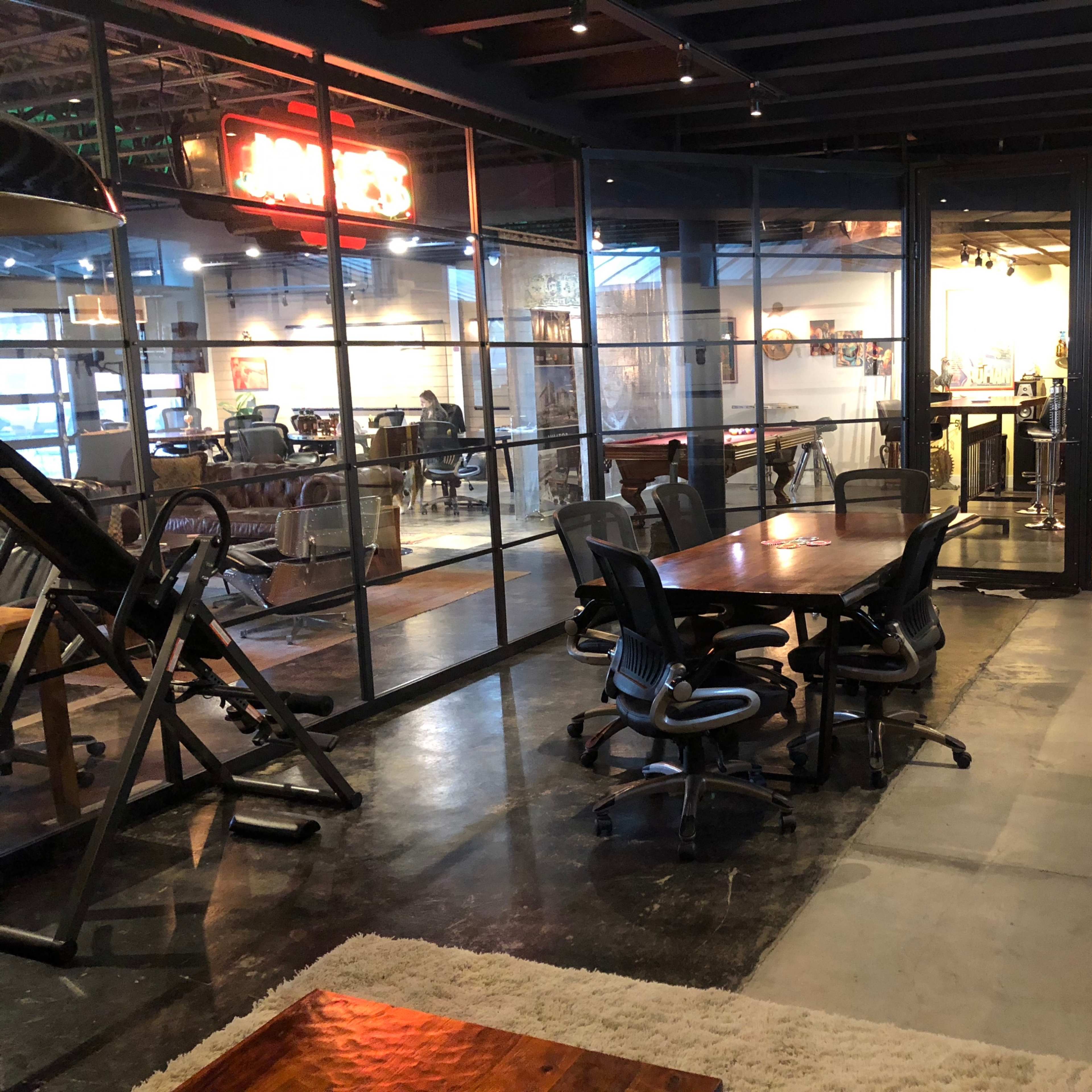 A modern interior features a glass-walled meeting room with a wooden table and black office chairs, adjacent to a cozy lounge area.