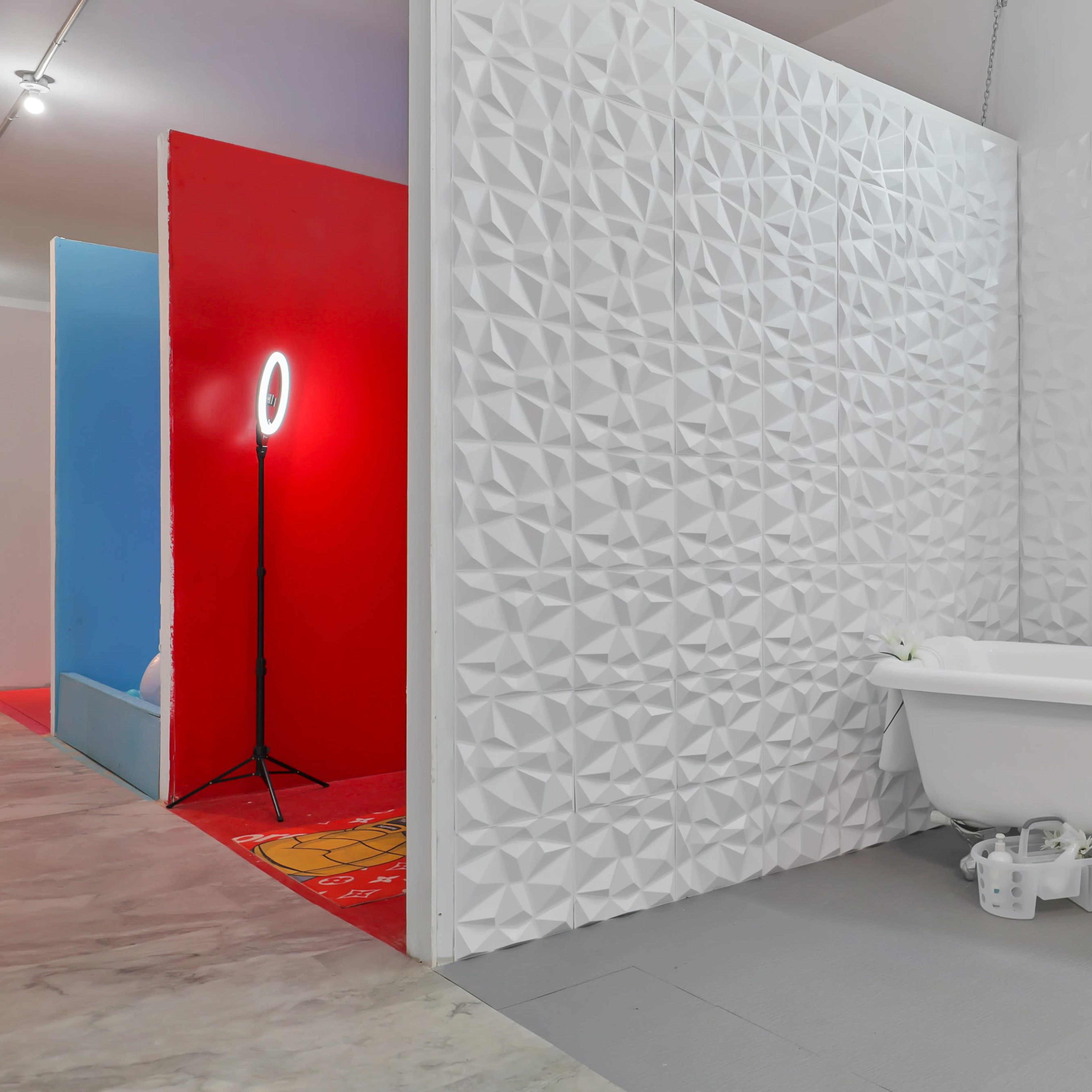 A bright bathroom setup with a freestanding bathtub against a textured white wall, accompanied by a ring light on a tripod.