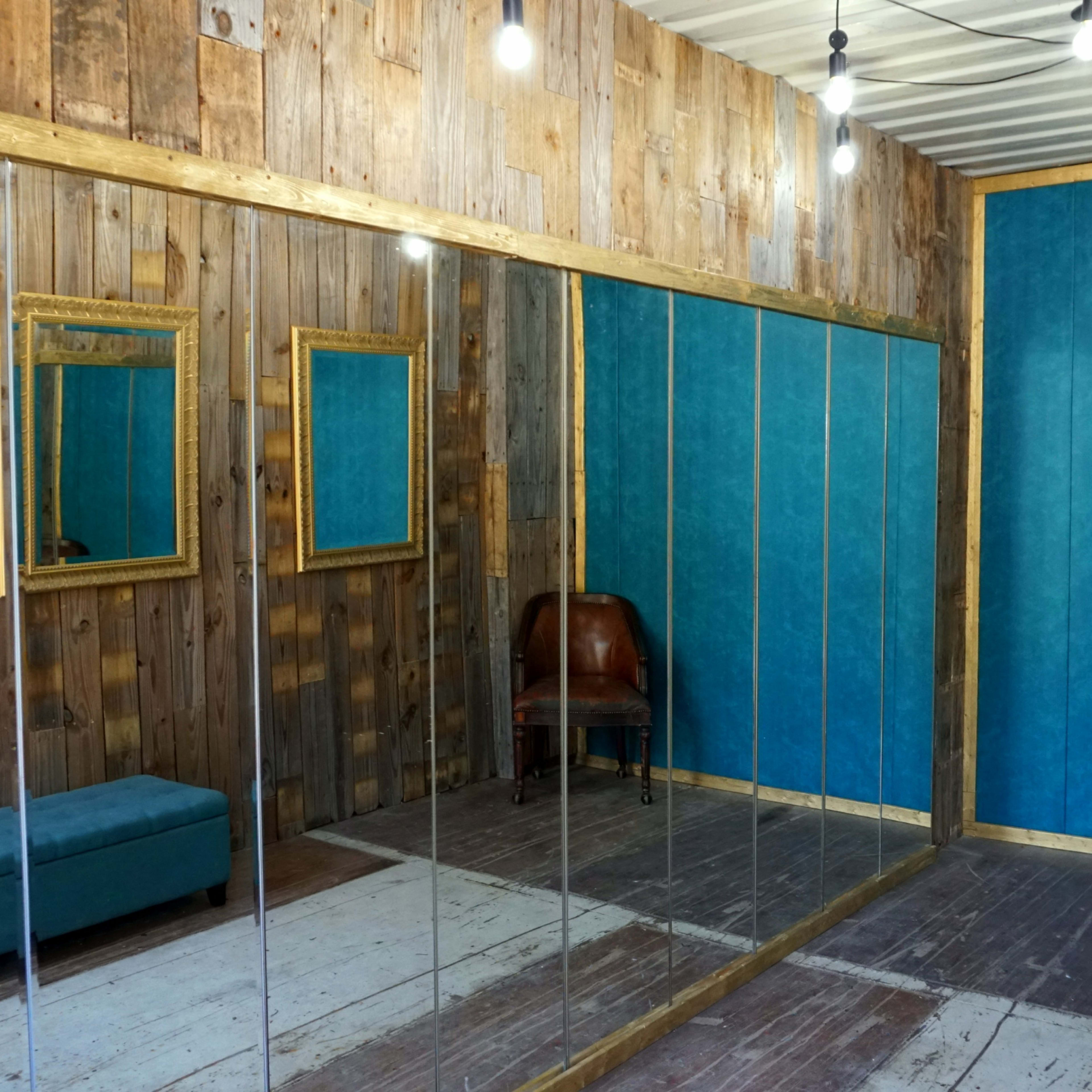 A room with wooden walls, two mirrors, a blue accent wall, a bench, and a brown chair.