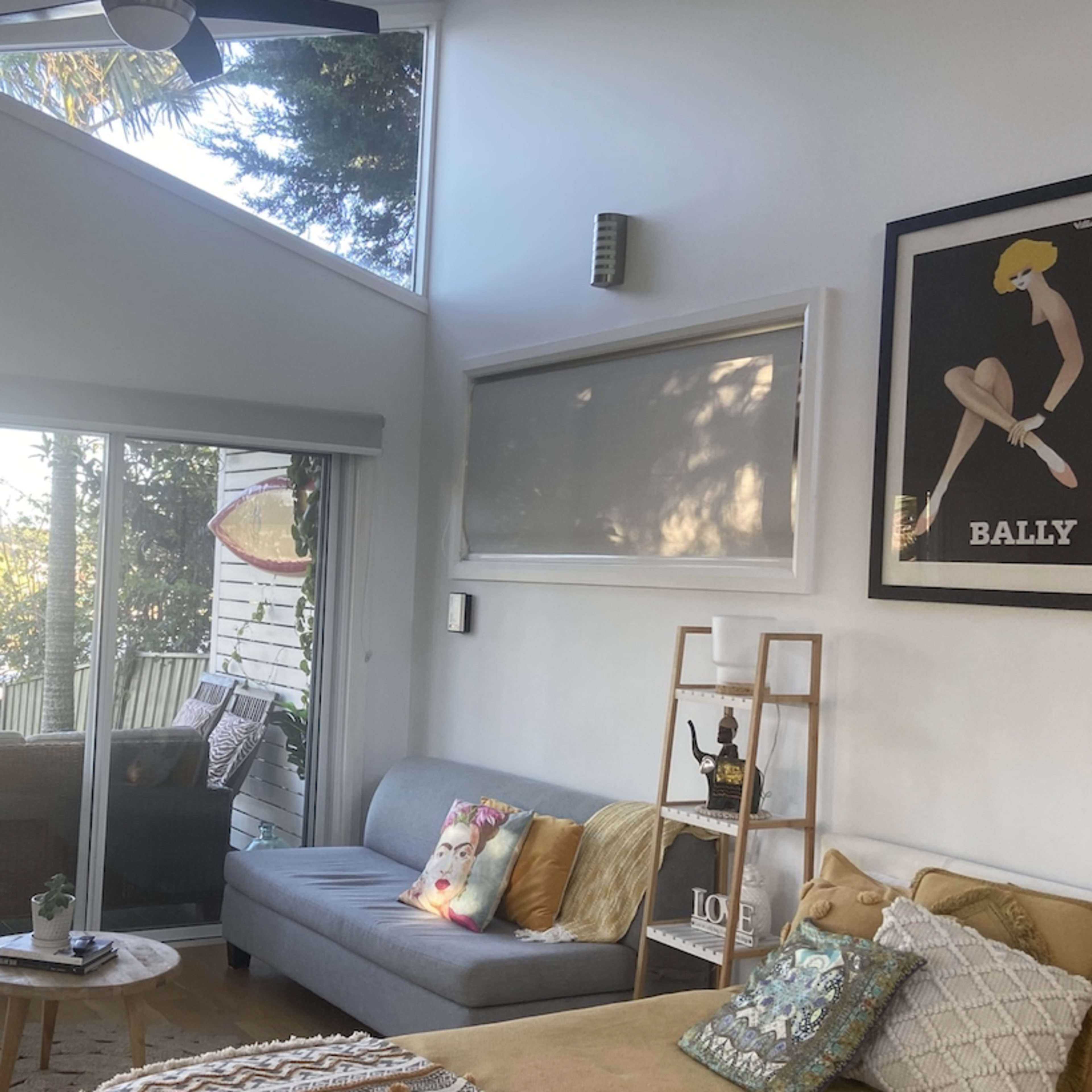 A modern living room with a gray sofa, a coffee table, and large windows revealing a view of greenery outside.