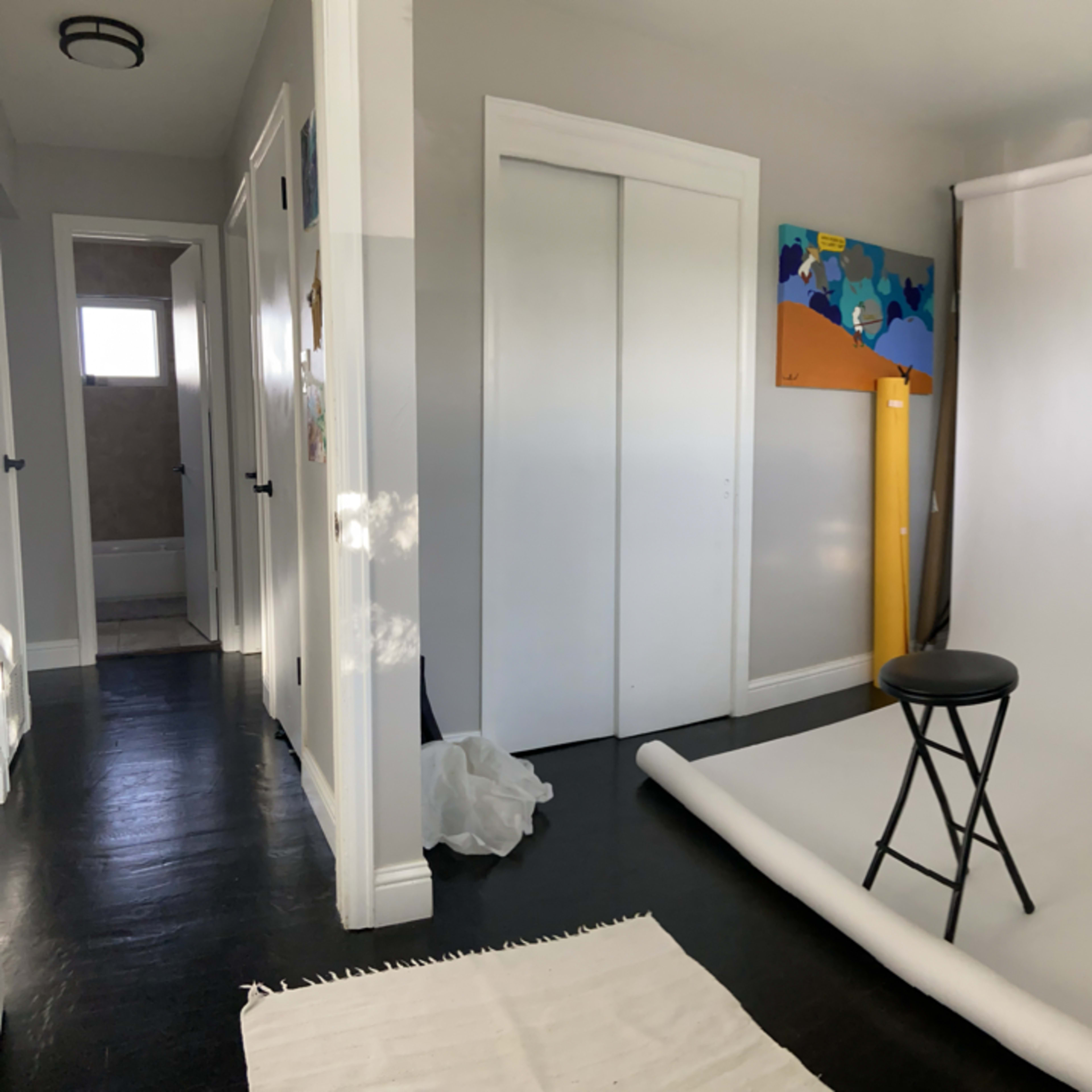 A photography studio featuring a white backdrop, a black stool, and colorful artwork on the wall.