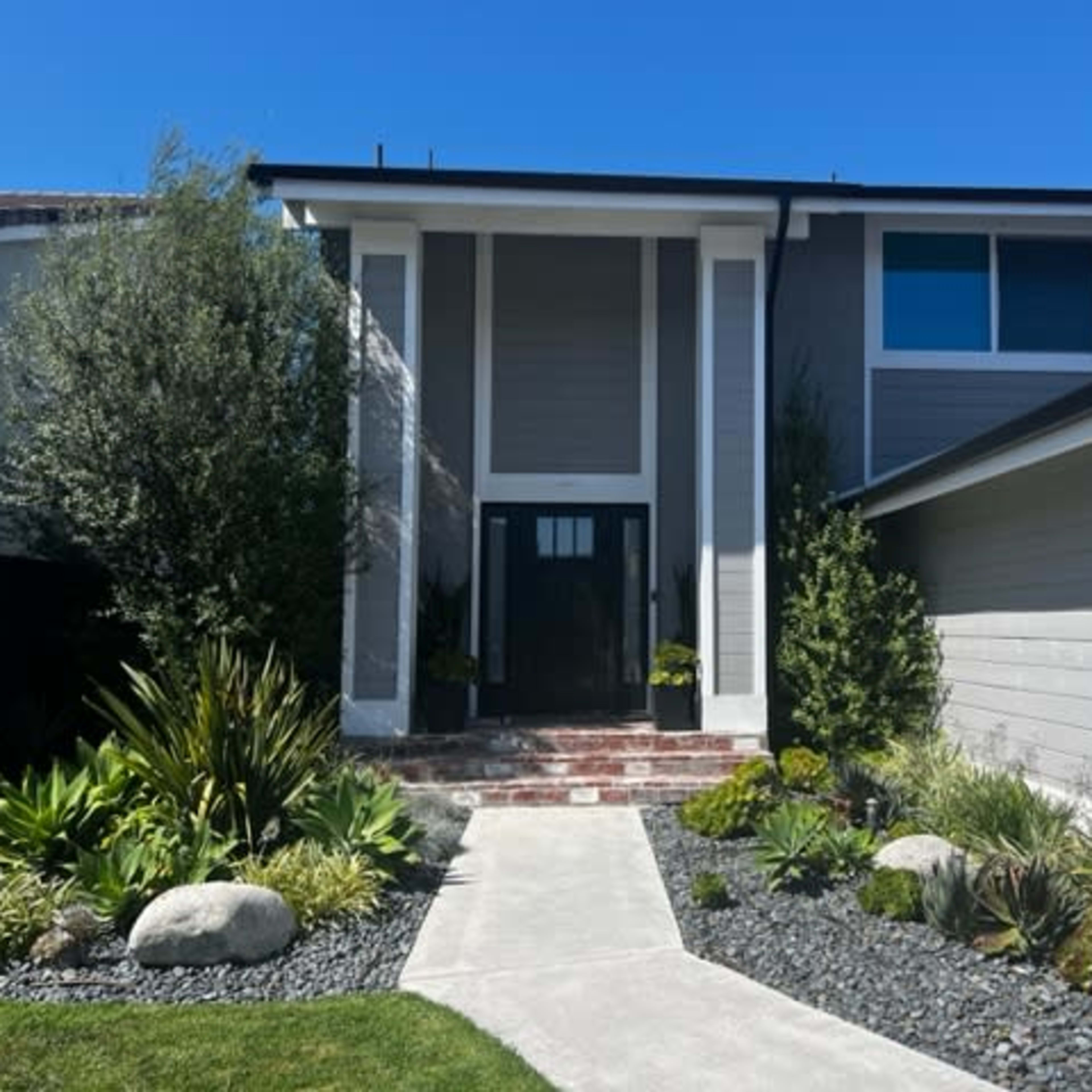A modern house with a prominent entrance flanked by landscaped greenery and stone pathways.