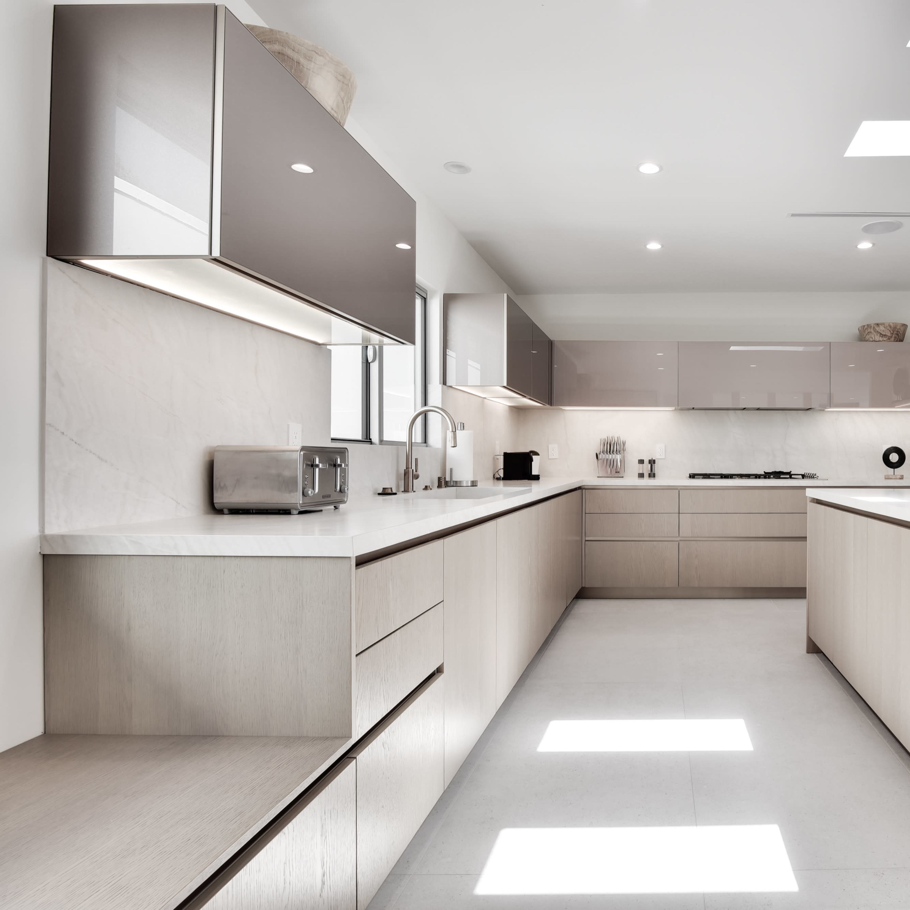 A modern kitchen features sleek cabinetry, a large island with a minimalist design, and ample natural light from skylights.