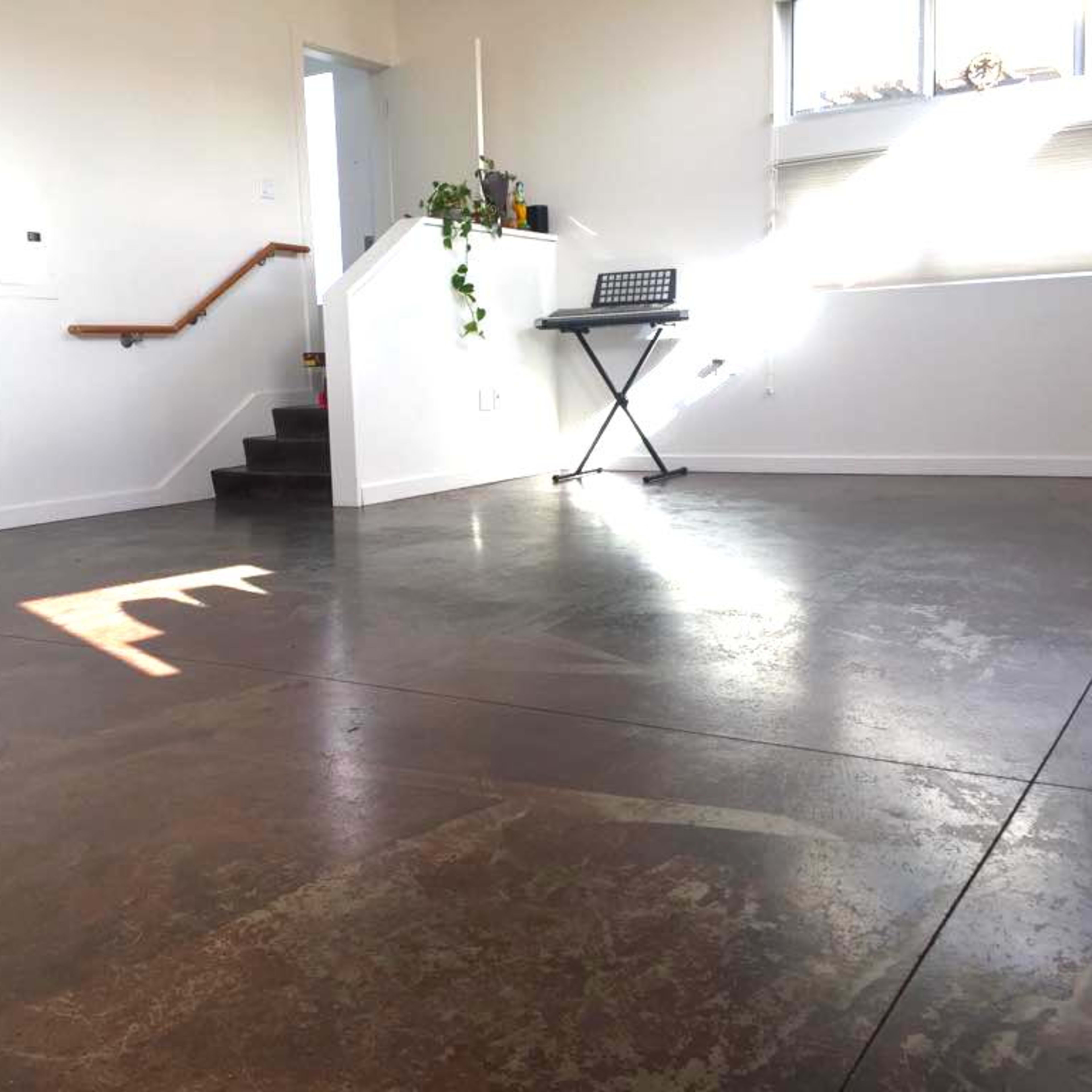 A spacious room with polished concrete flooring, a set of stairs leading to an upper level, and a keyboard stand against the wall.