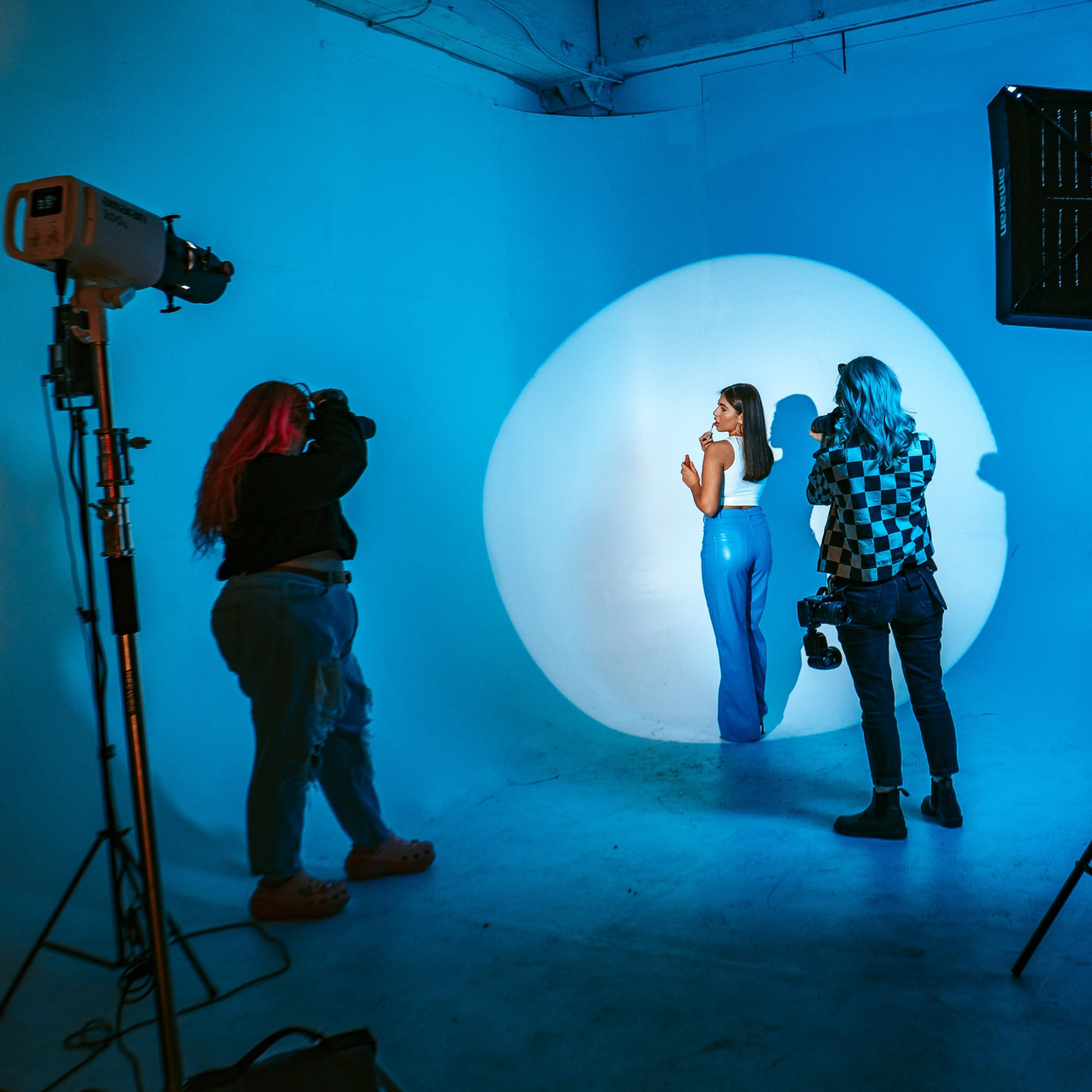 A model poses in a blue-lit studio while photographers capture images using professional equipment.