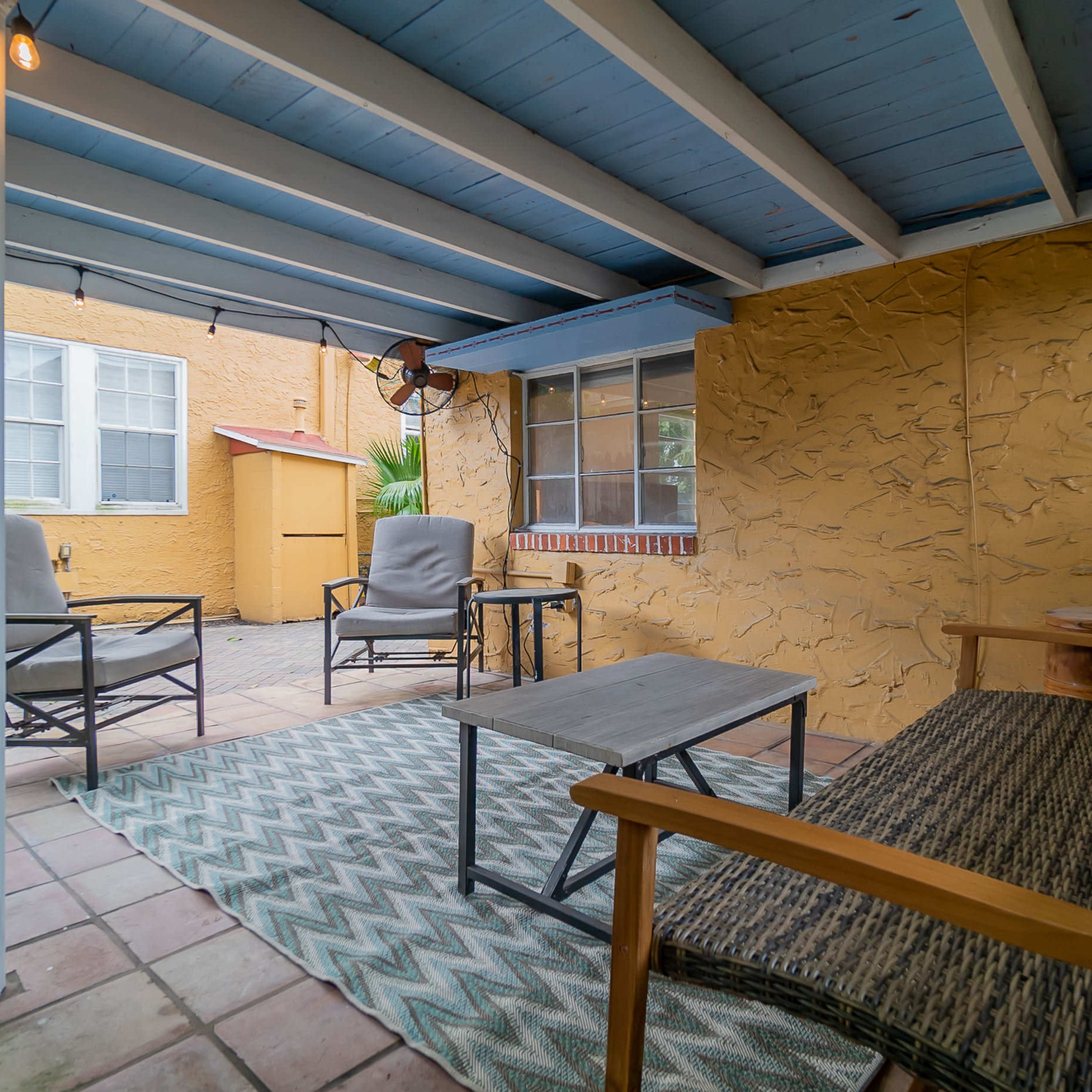 A covered outdoor seating area with a small table and several chairs on a tiled patio.