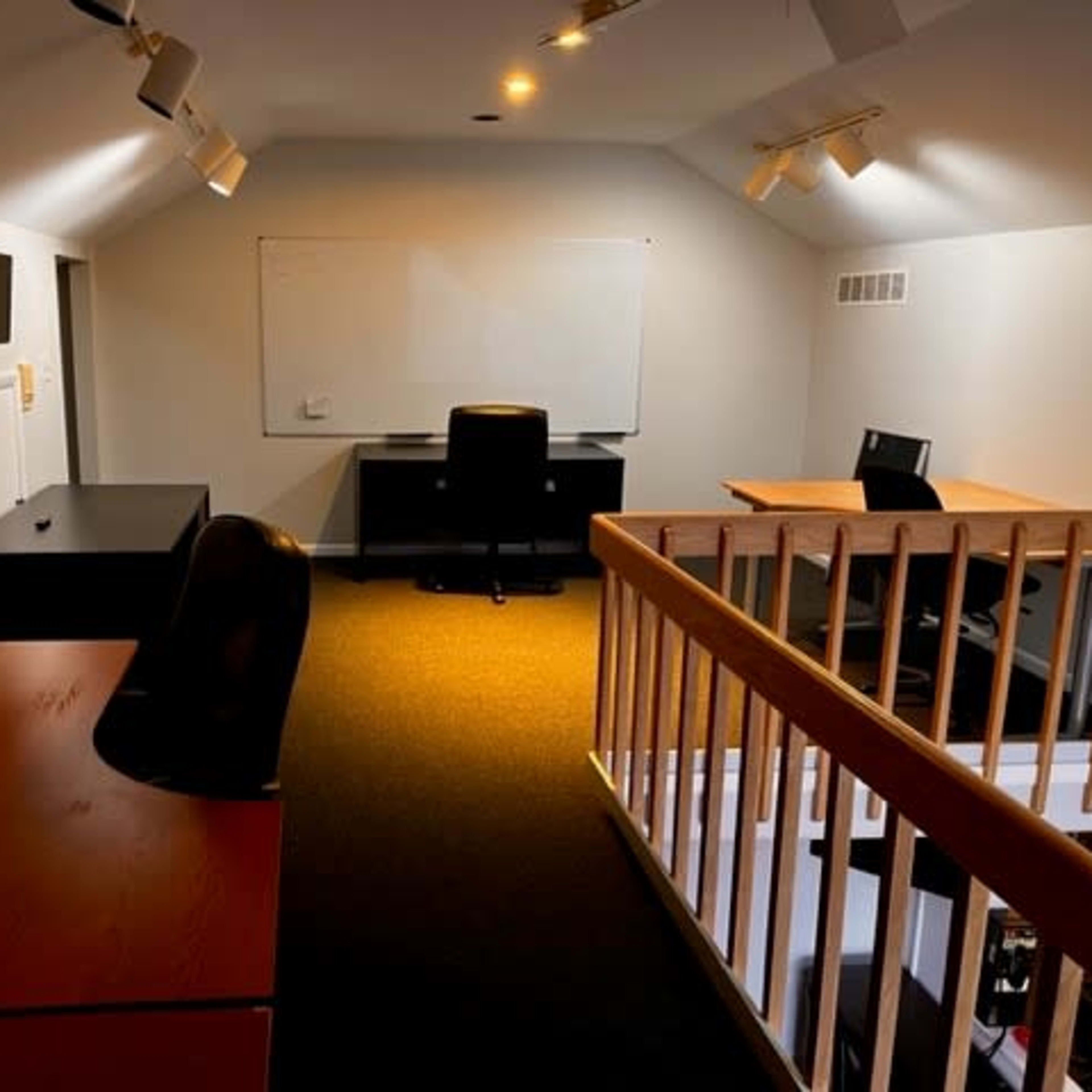 A well-lit office space featuring black and wooden desks, office chairs, and a whiteboard on the wall.