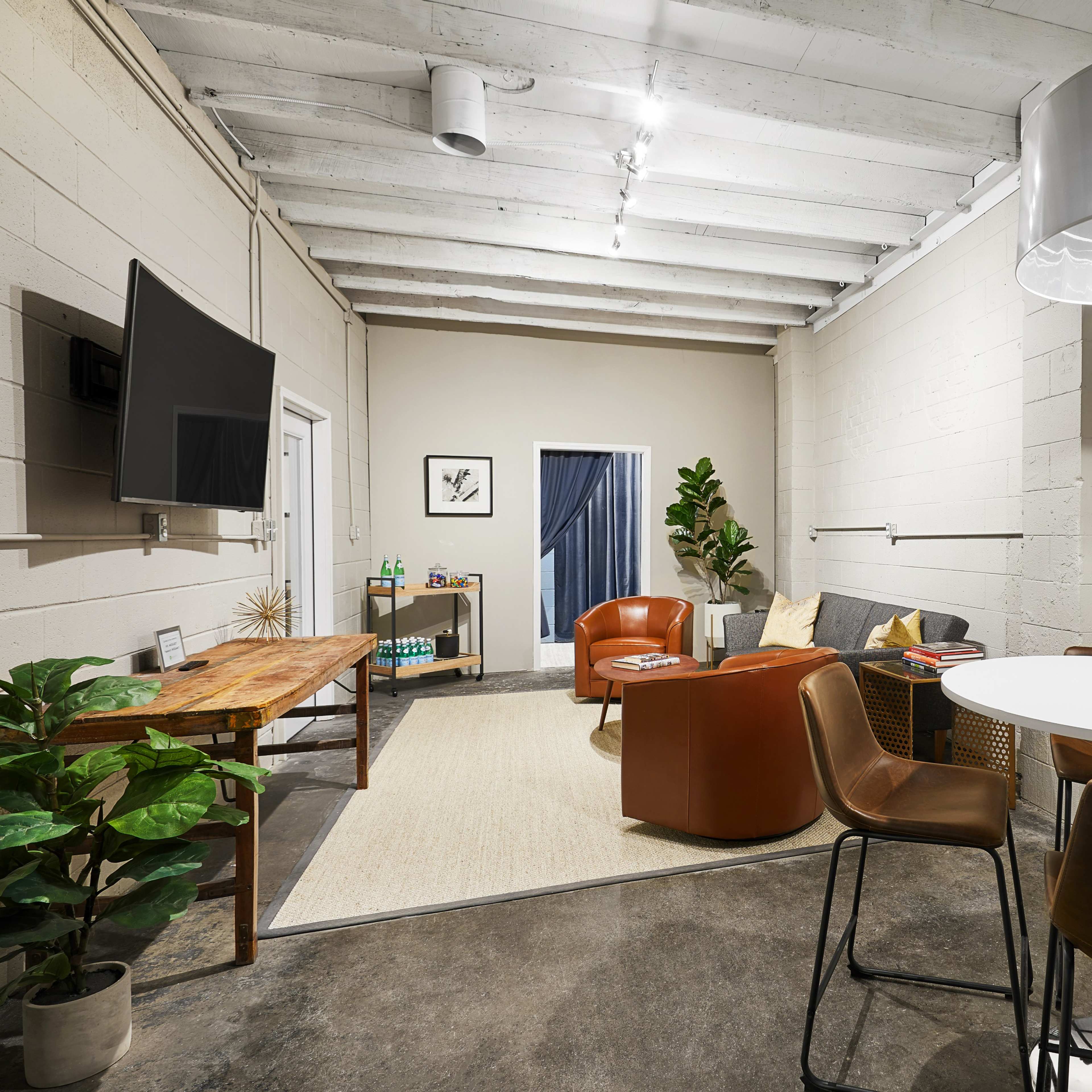 A contemporary office space with a circular table and chairs, a couch, a wooden table, and a large light fixture overhead.