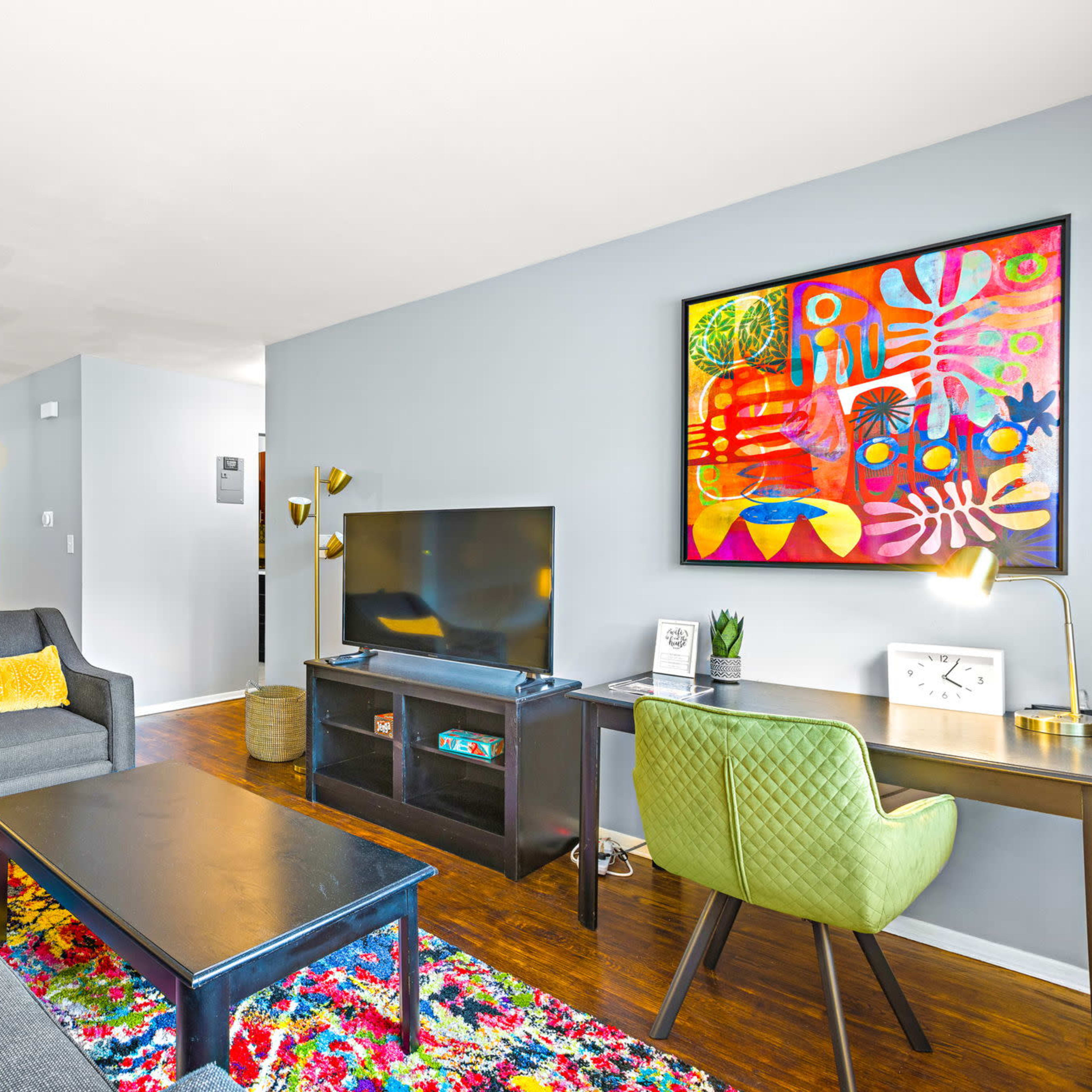 A modern living room with a colorful area rug, a television, a desk, and vibrant artwork on the wall.