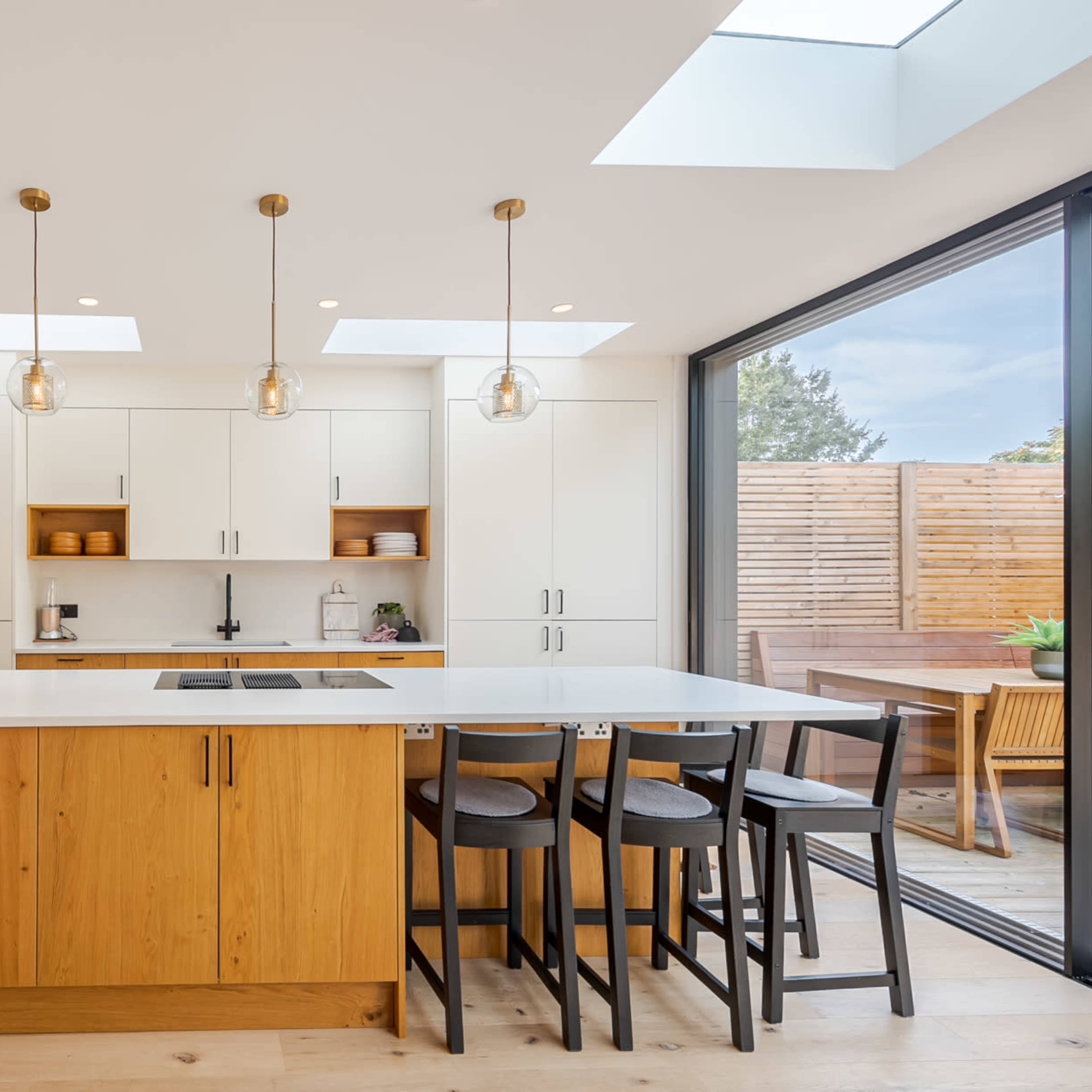 The kitchen features a central island with wooden cabinetry, overhead pendant lights, and large windows that provide natural light.