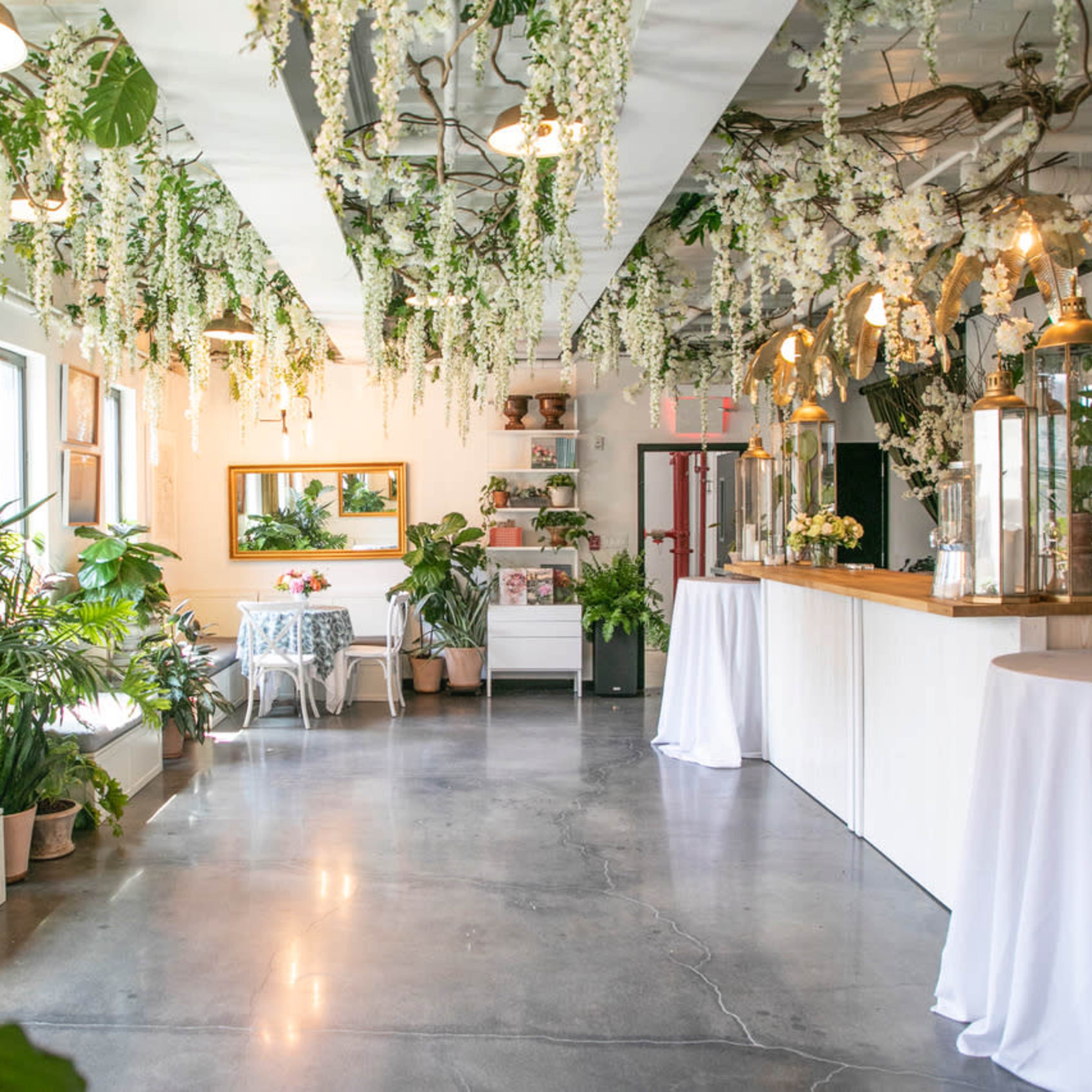 A bright indoor space adorned with hanging flowers and greenery, featuring seating areas and a wooden counter.