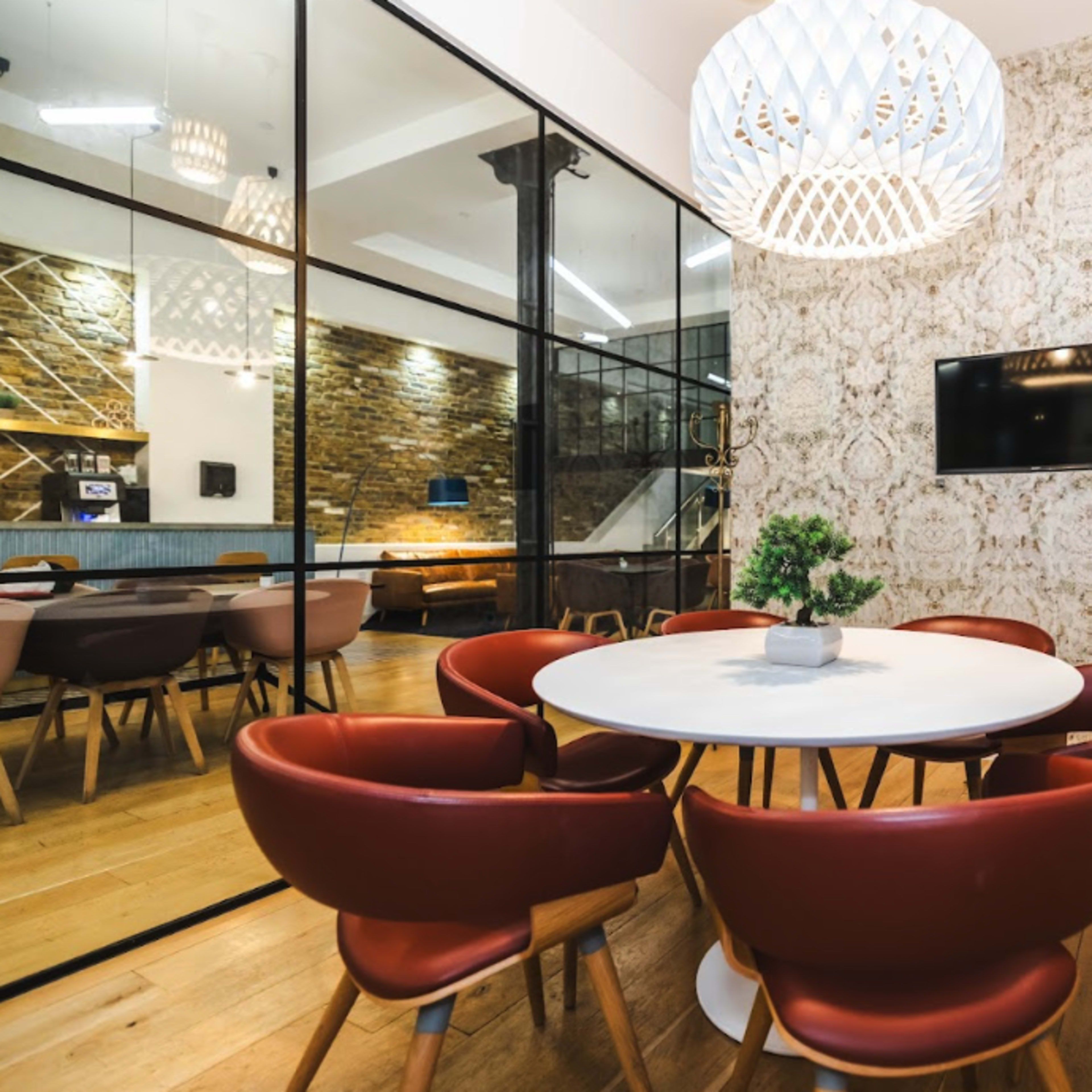 A modern meeting room features a round table surrounded by leather chairs, with a decorative wall and a pendant light above.