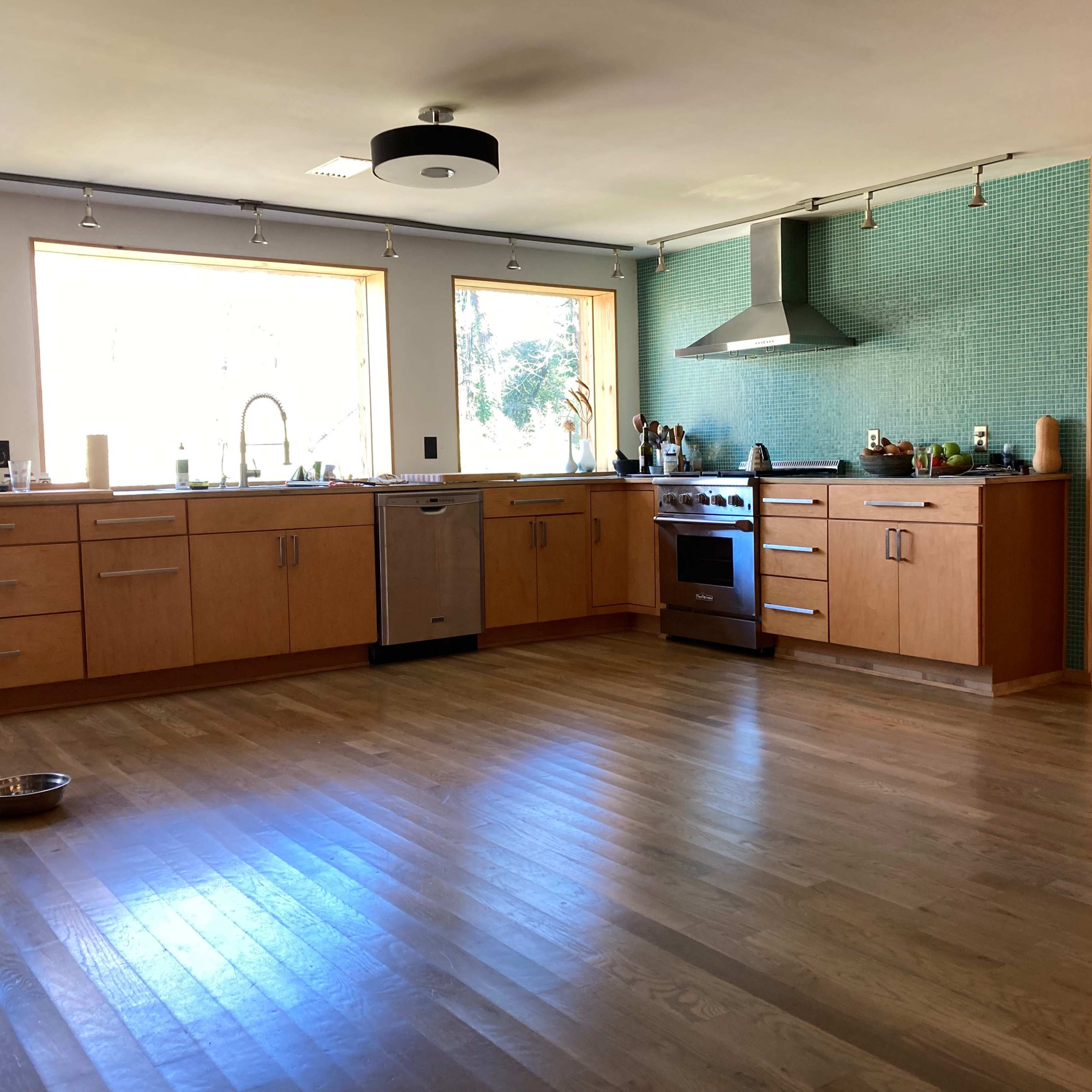 A modern kitchen with wooden cabinets, a stainless steel stove, and large windows allowing natural light.
