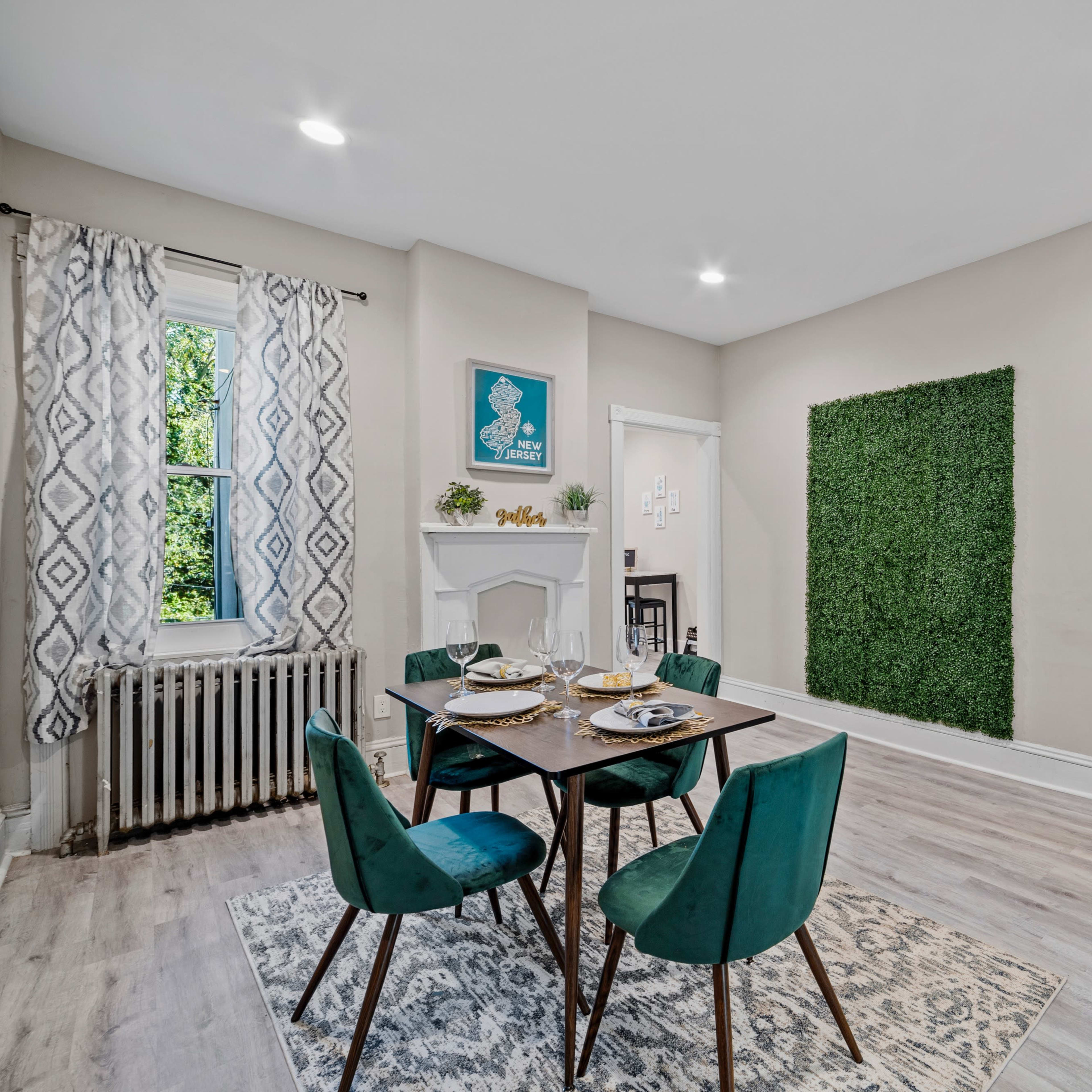A dining area with a table set for four, surrounded by teal chairs, a window providing natural light, and a wall covered in greenery.