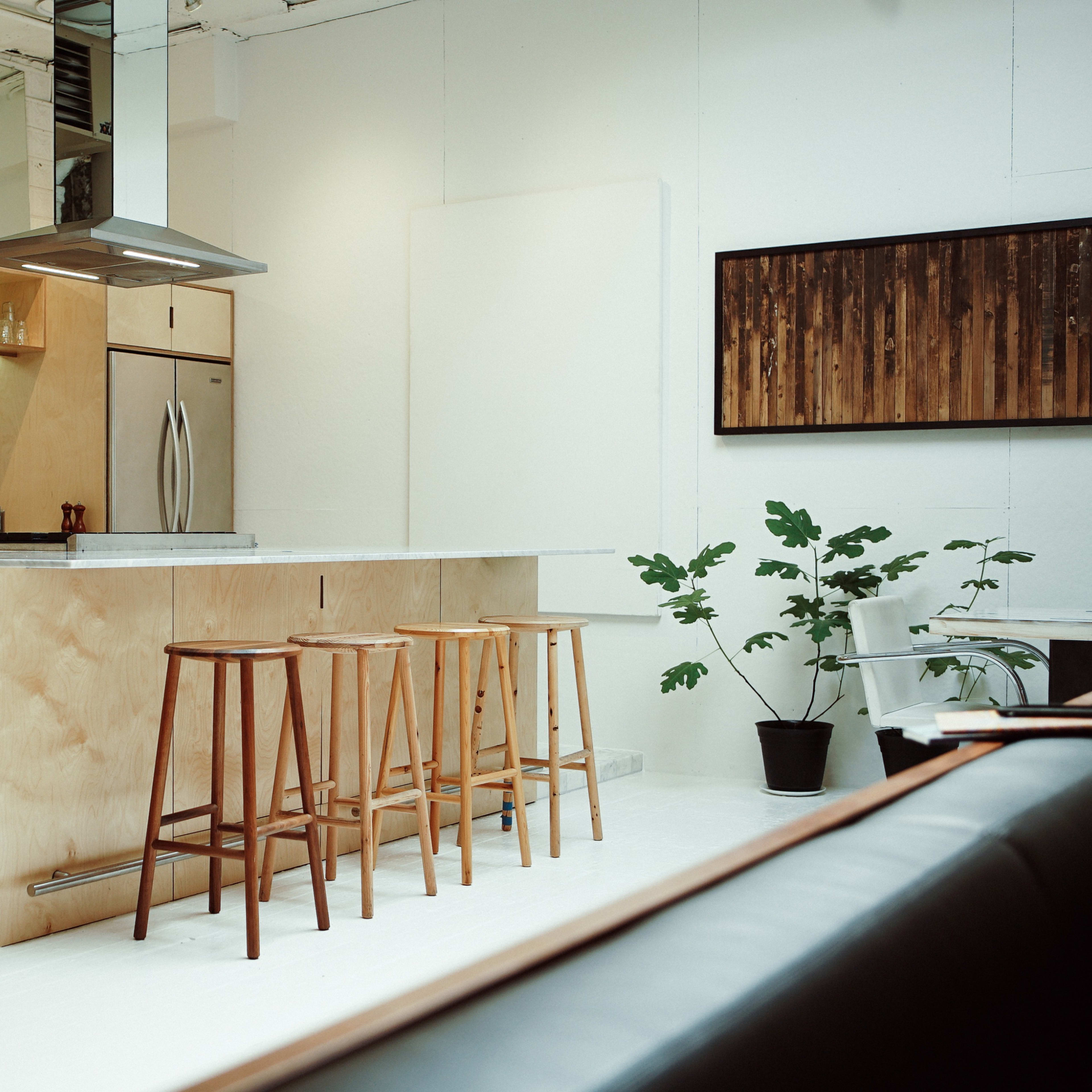 A modern kitchen featuring a central island with three wooden stools, stainless steel appliances, and a white tiled backsplash.