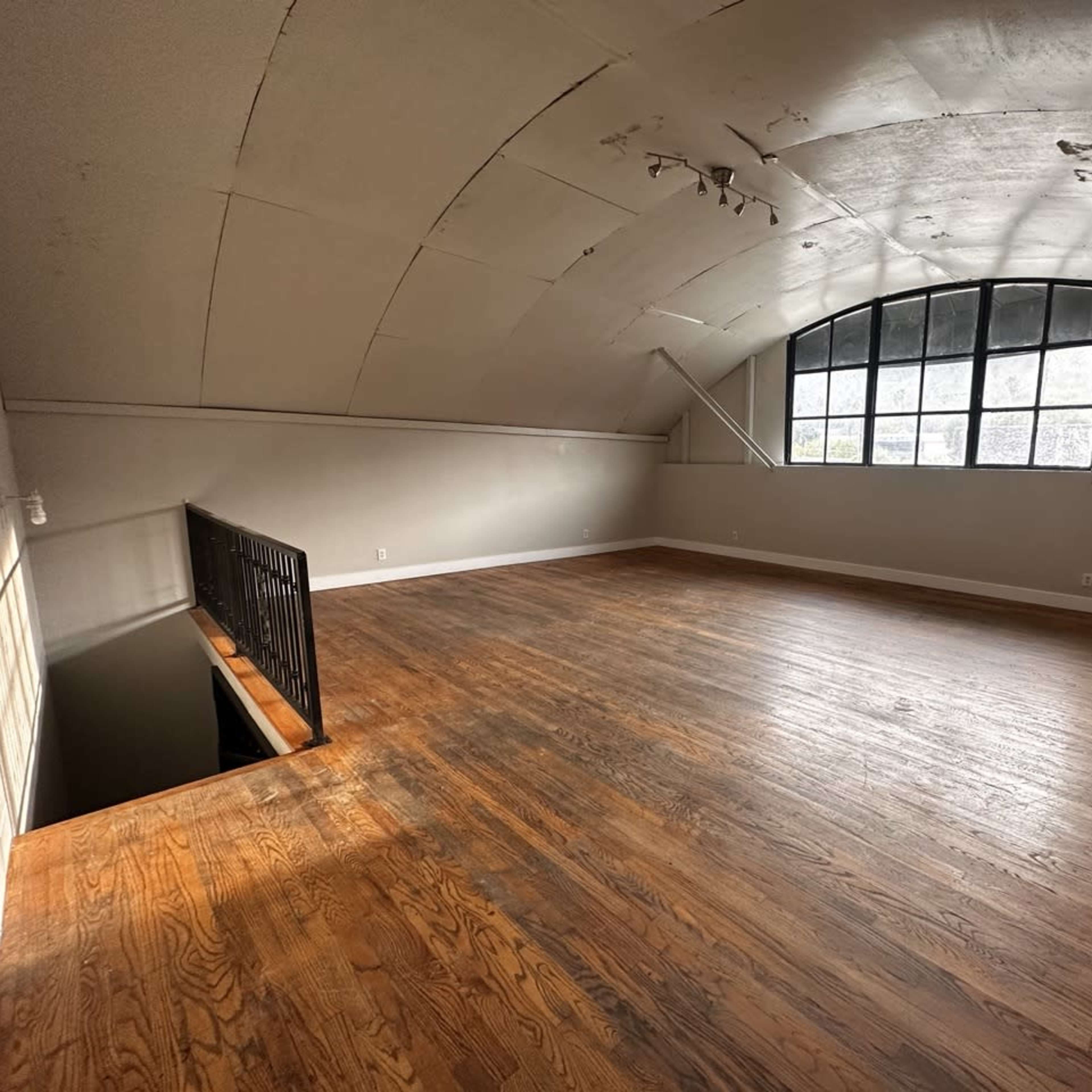A spacious, empty room with wooden flooring and large arched windows along one wall.