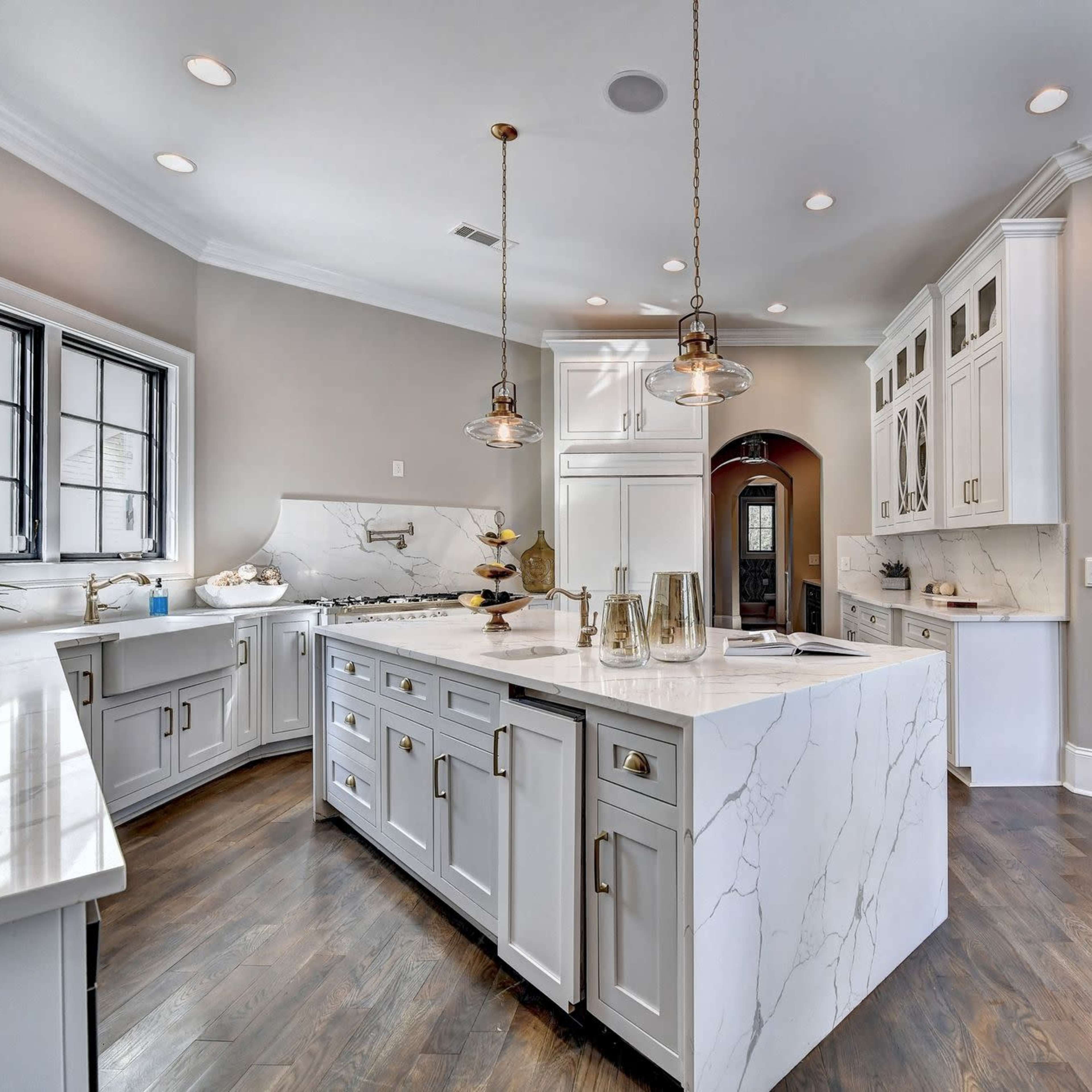 A modern kitchen featuring a large marble island, white cabinetry, and pendant lighting.