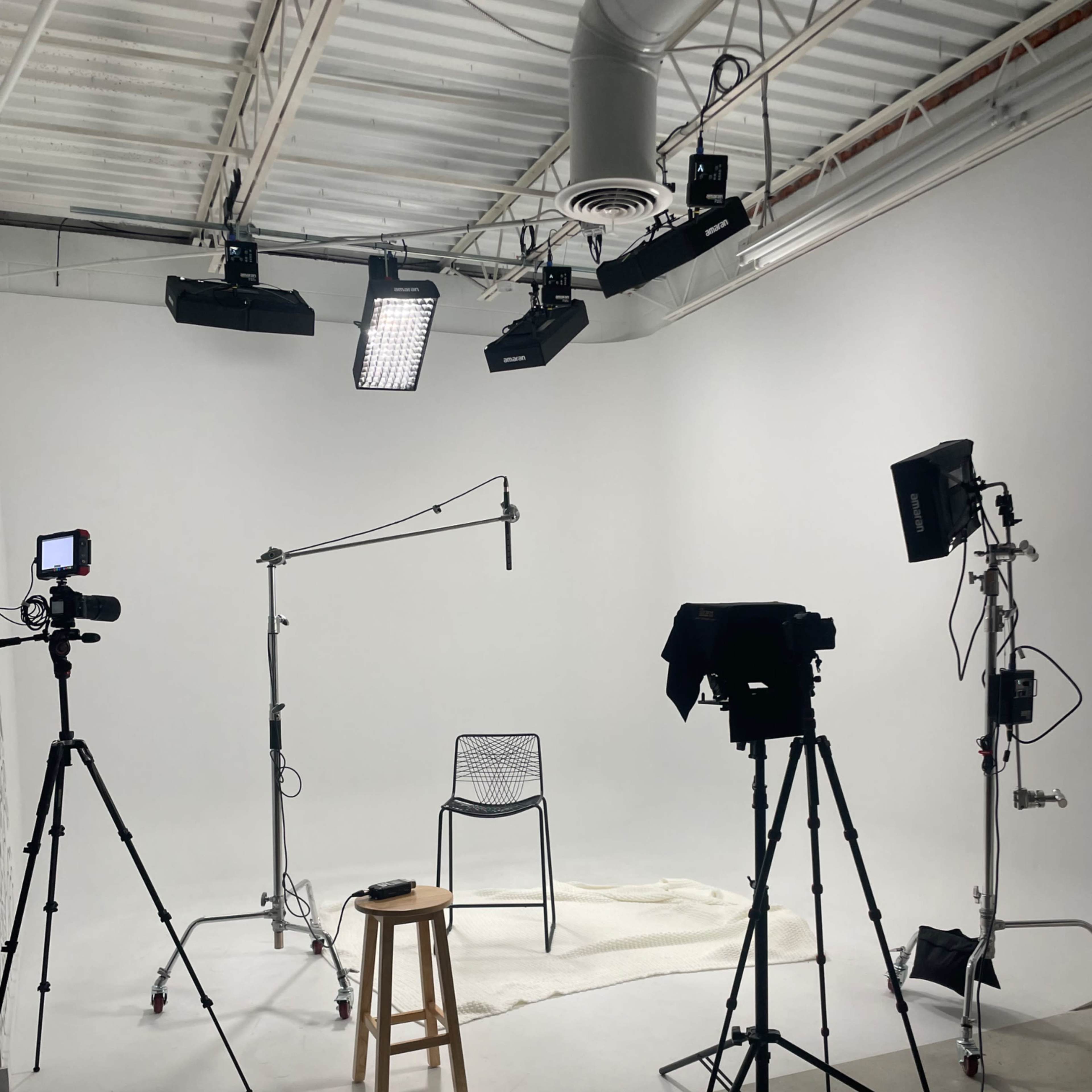 A minimalist filming studio features a single chair on a rug, surrounded by cameras and lighting equipment.