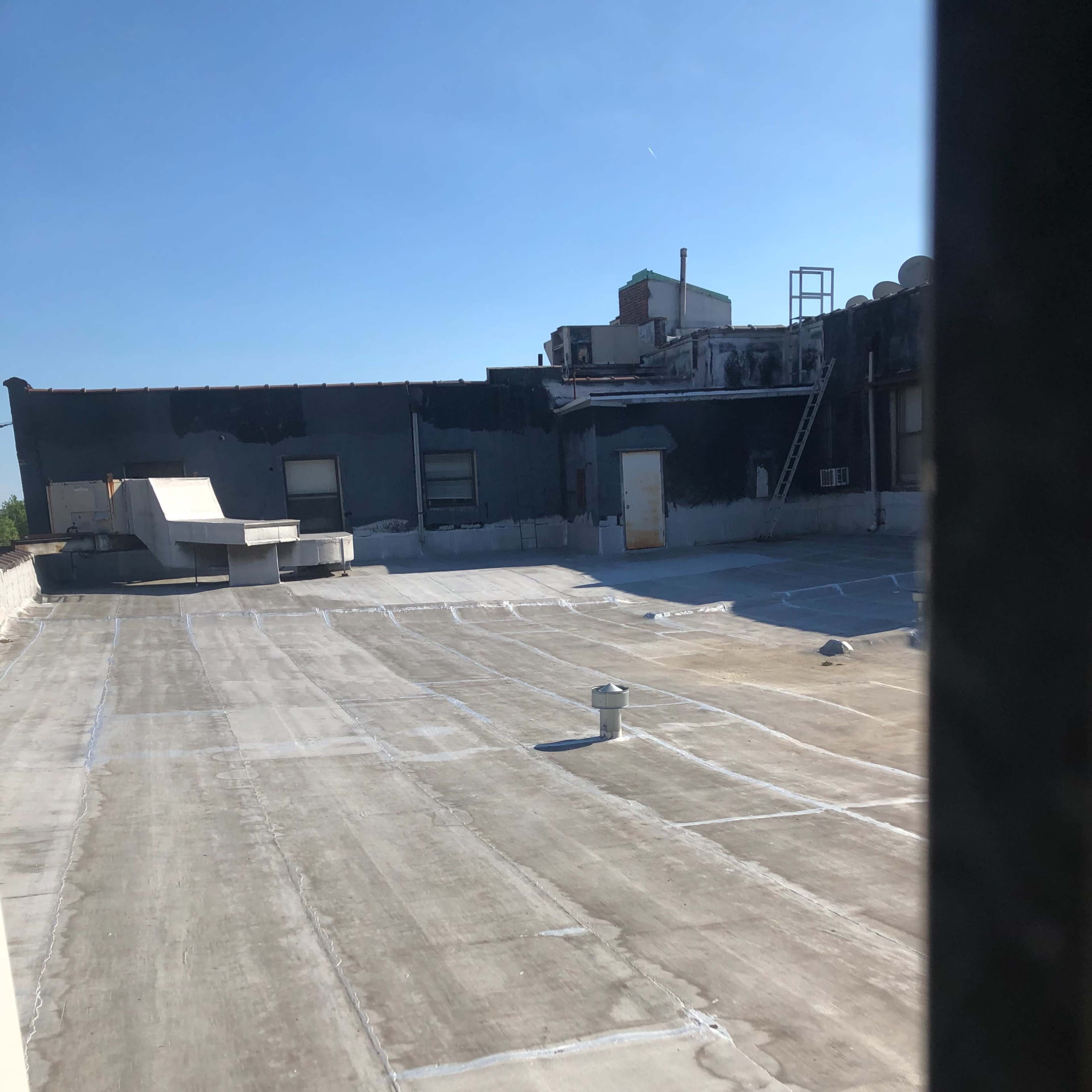 A flat rooftop with a light-colored surface, some scattered objects, and a clear blue sky overhead.