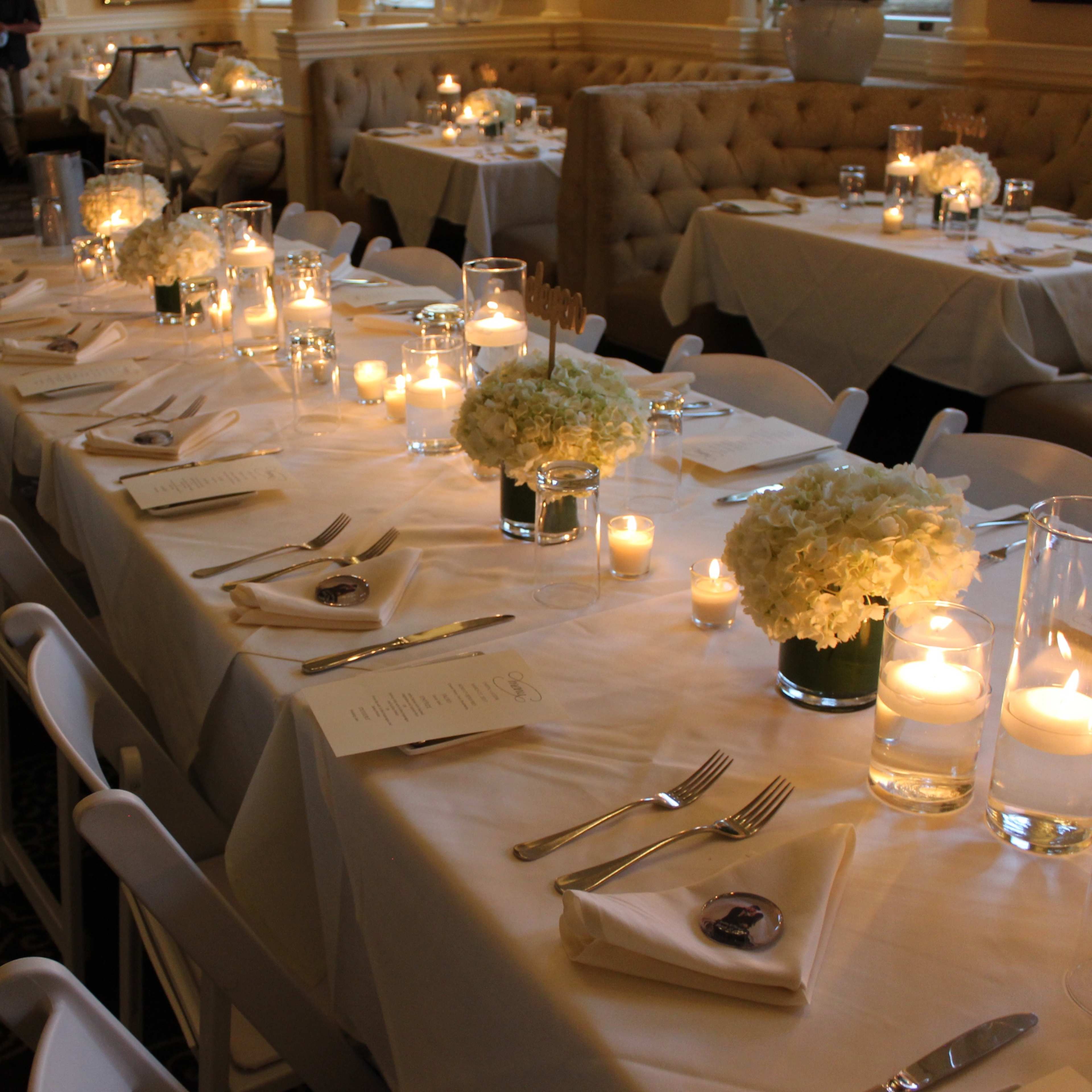 A dining setup with elegantly arranged tables featuring white tablecloths, floral centerpieces, and candles.