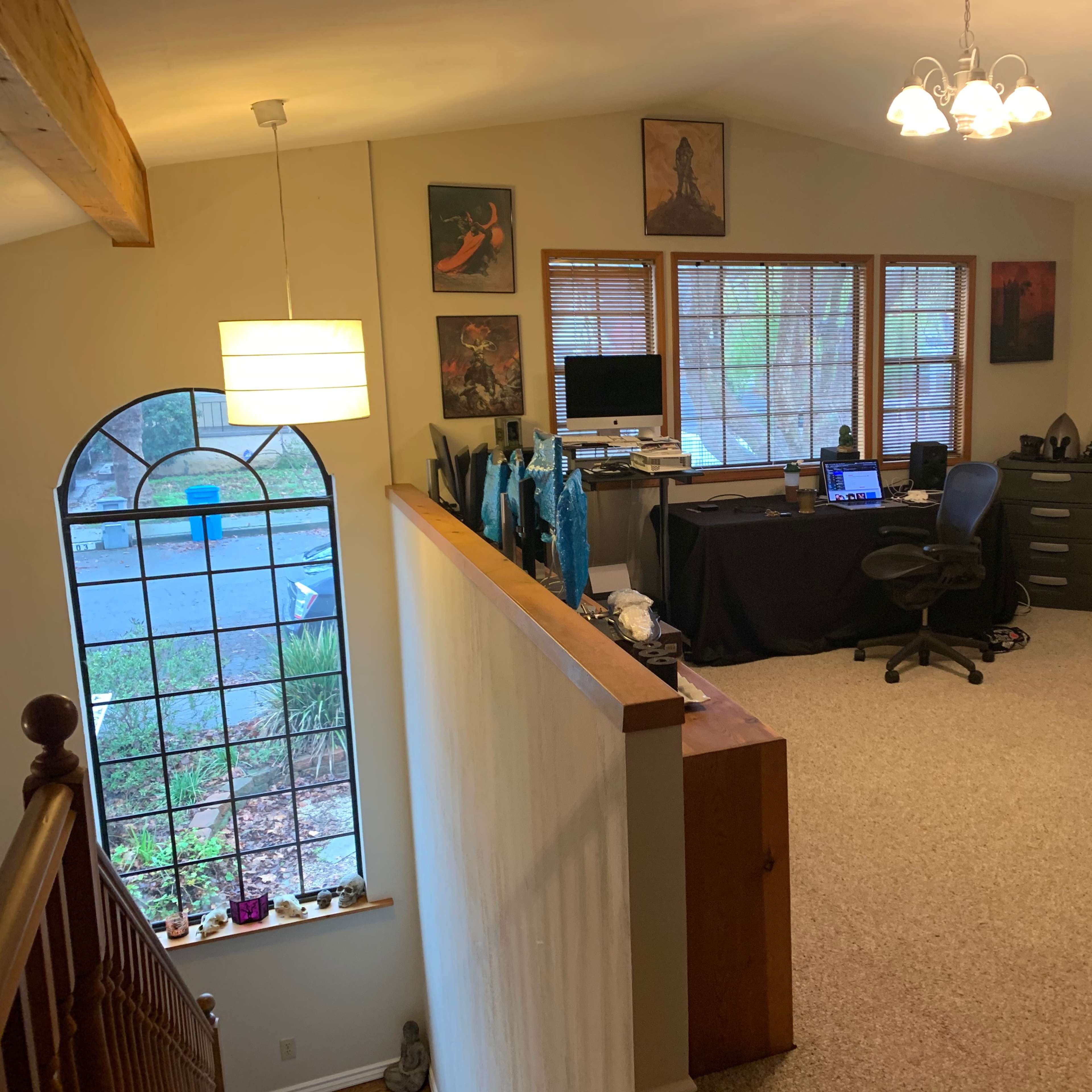 A home office area with a desk and computer, located in a well-lit room with carpeted flooring and several wall decorations.